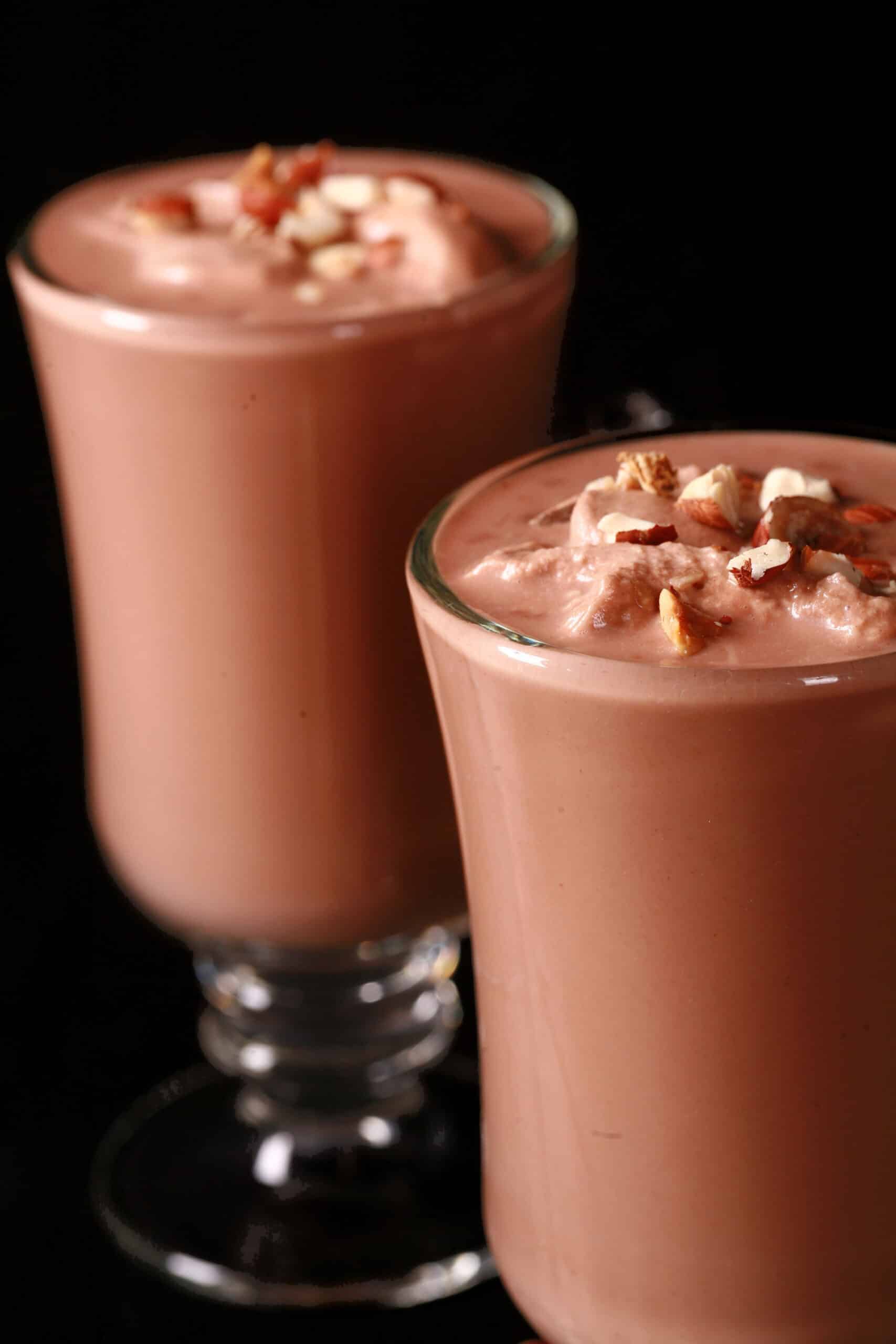 2 glass mugs of nutella hot cocoa, topped with nutella whipped cream and chopped hazelnuts.