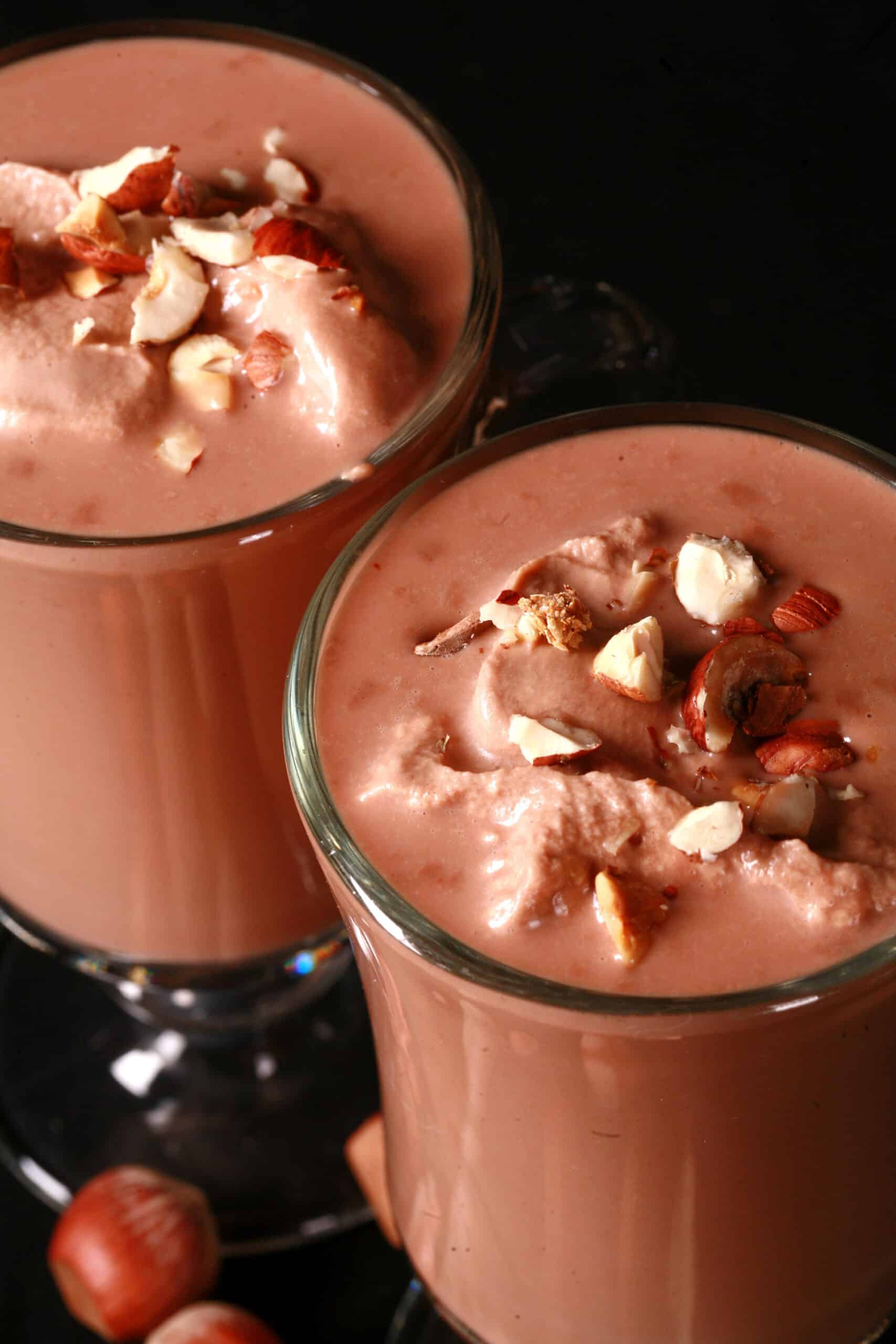 2 glass mugs of nutella hot chocolate, topped with nutella whipped cream and chopped hazelnuts.