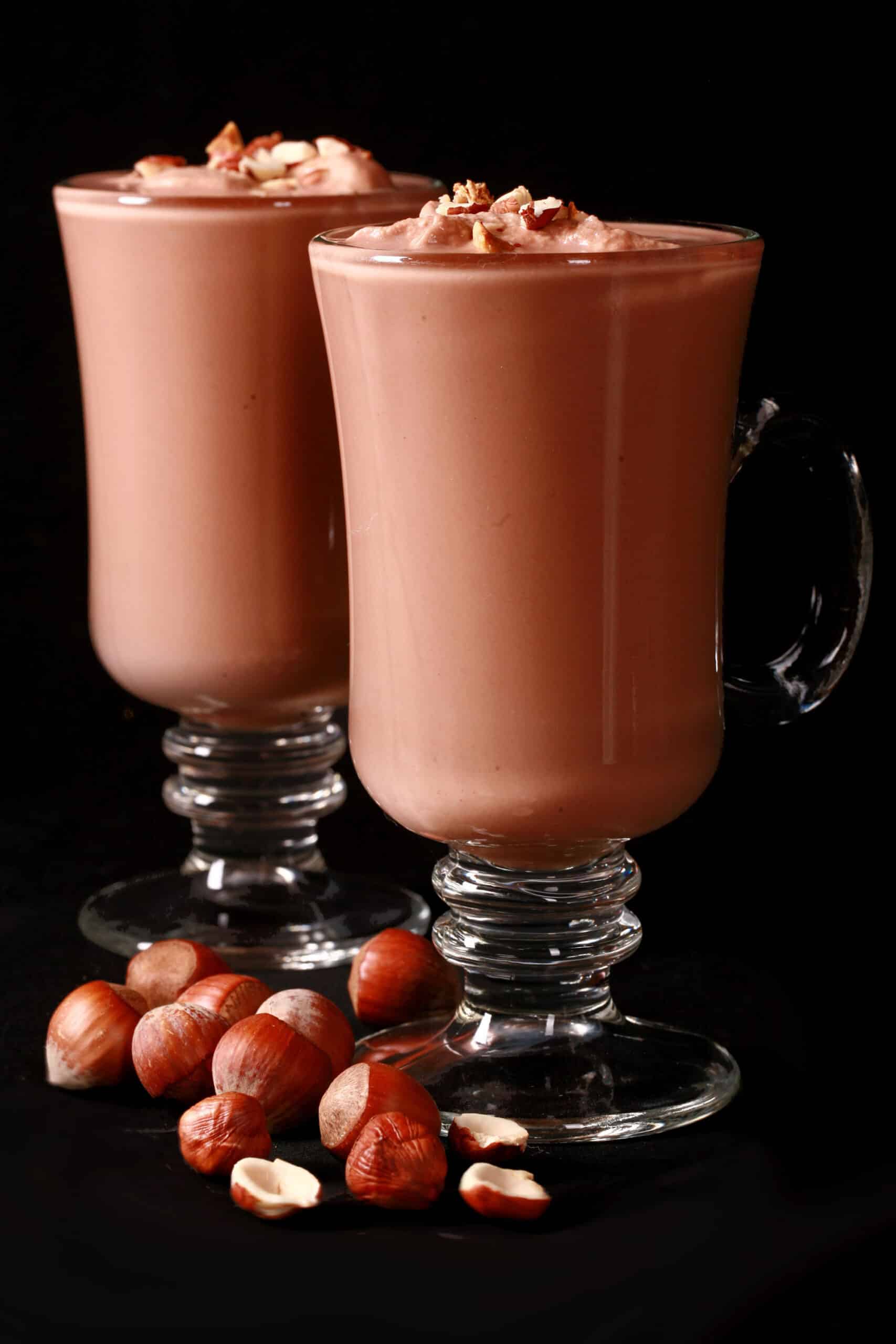 2 glass mugs of nutella hot cocoa, topped with nutella whipped cream and chopped hazelnuts.