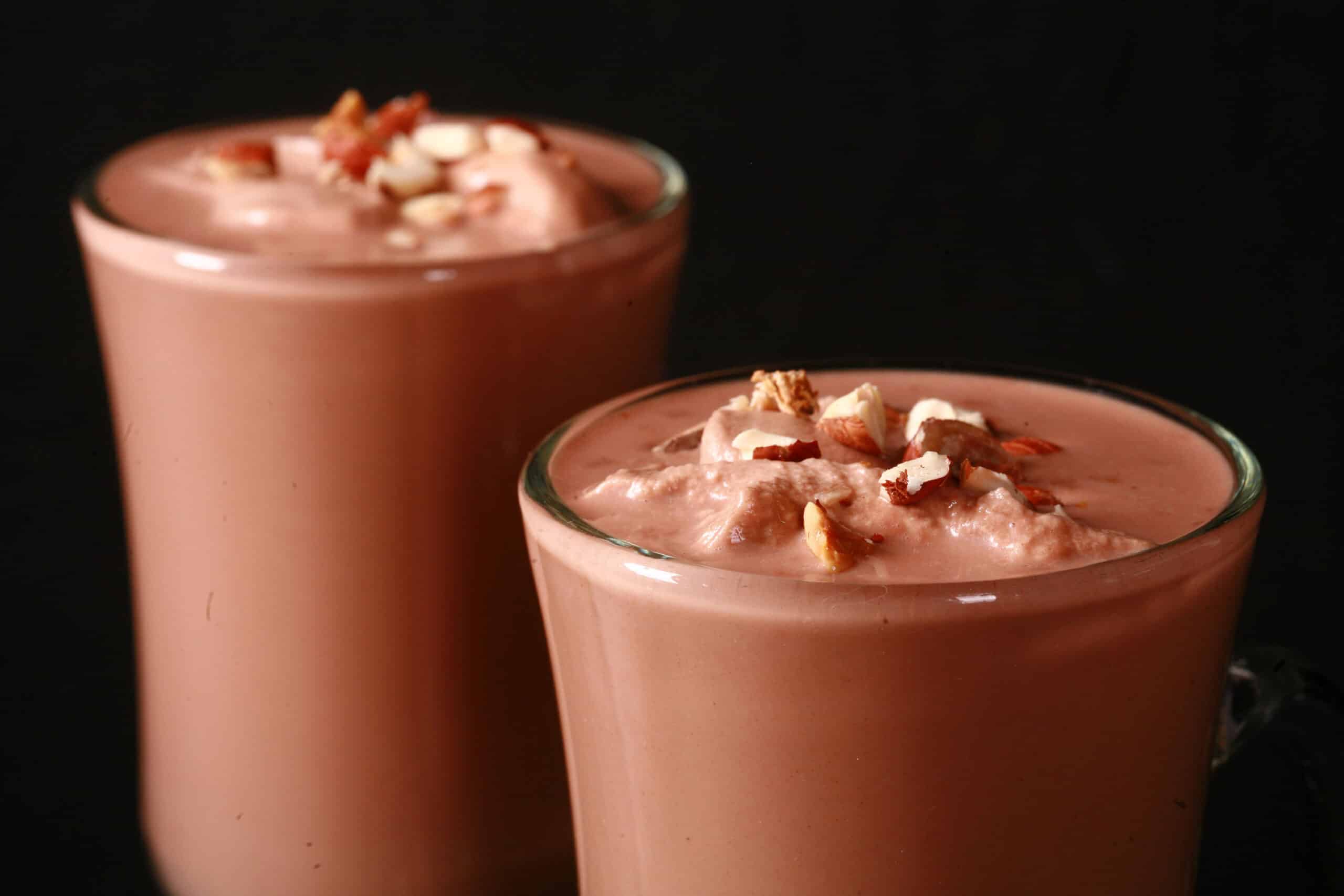 2 glass mugs of nutella hot cocoa, topped with nutella whipped cream and chopped hazelnuts.