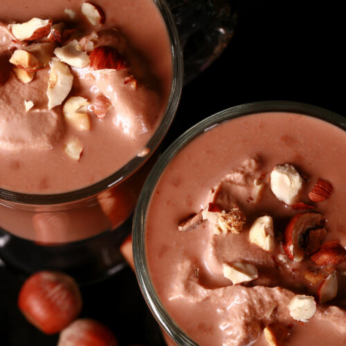 2 glass mugs of nutella hot chocolate, topped with nutella whipped cream and chopped hazelnuts.