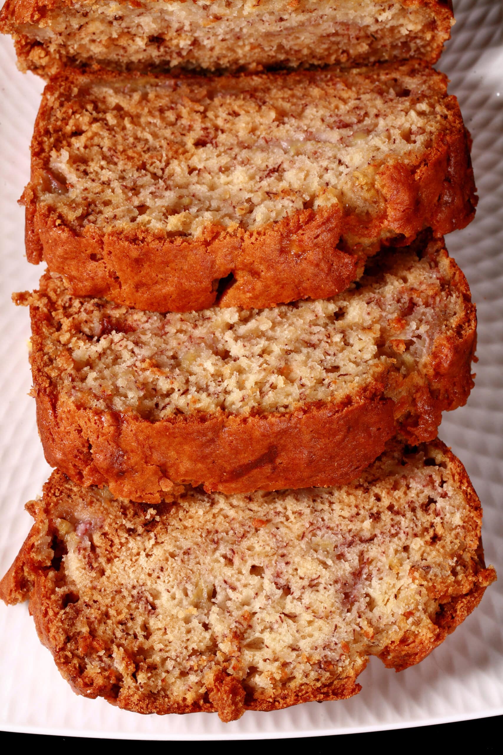 A sliced loaf of eggless banana bread on a white serving platter.