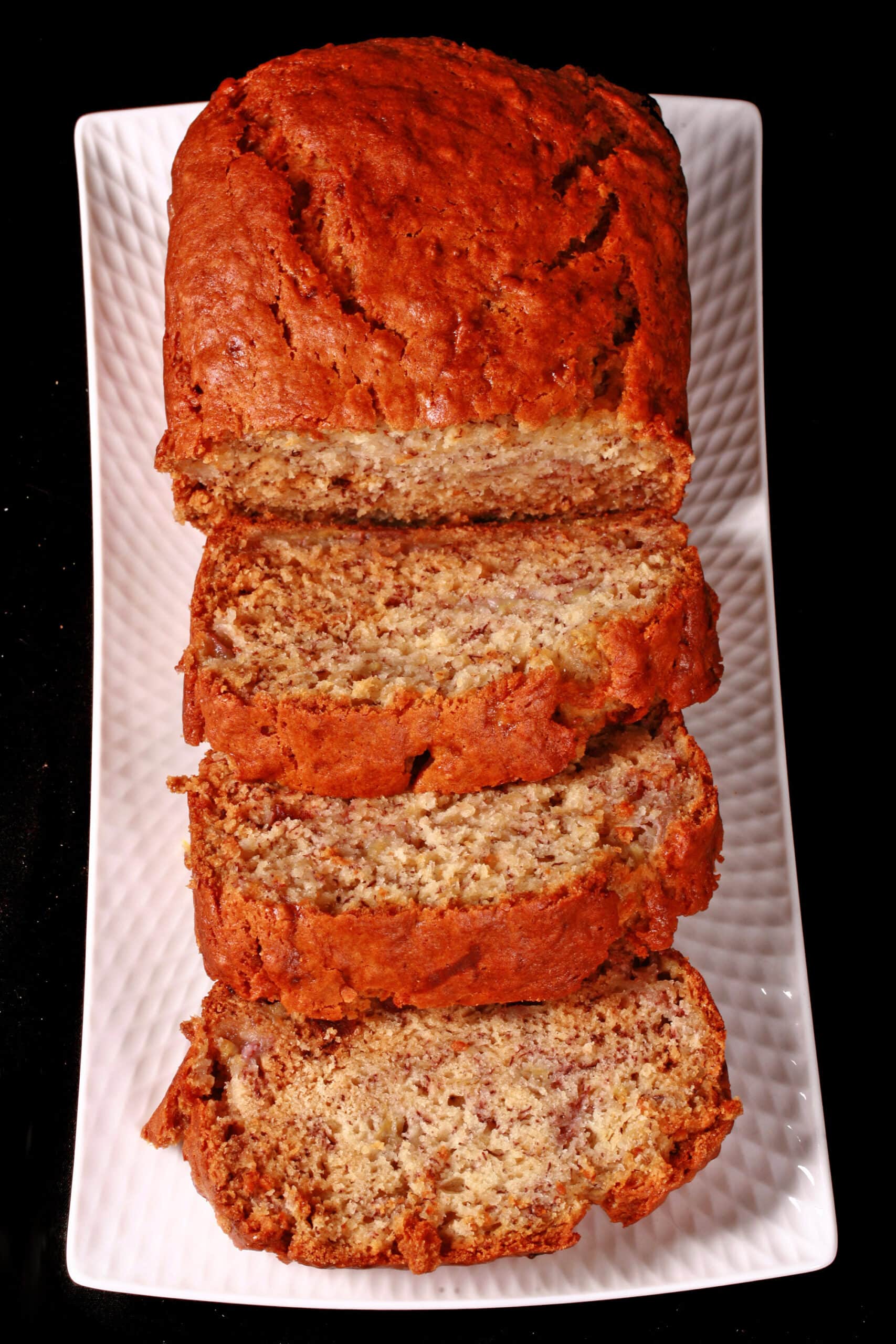 A sliced loaf of egg free banana bread on a white serving platter.