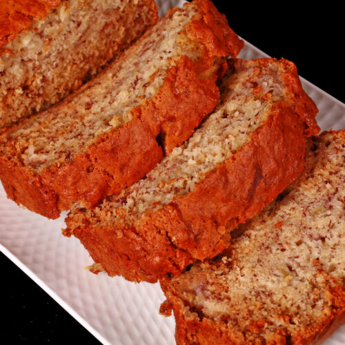 A sliced loaf of eggless banana bread on a white serving platter.