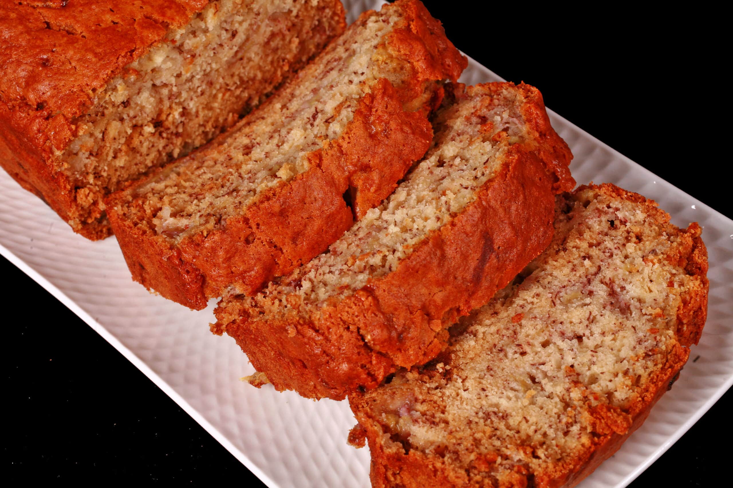 A sliced loaf of eggless banana bread on a white serving platter.