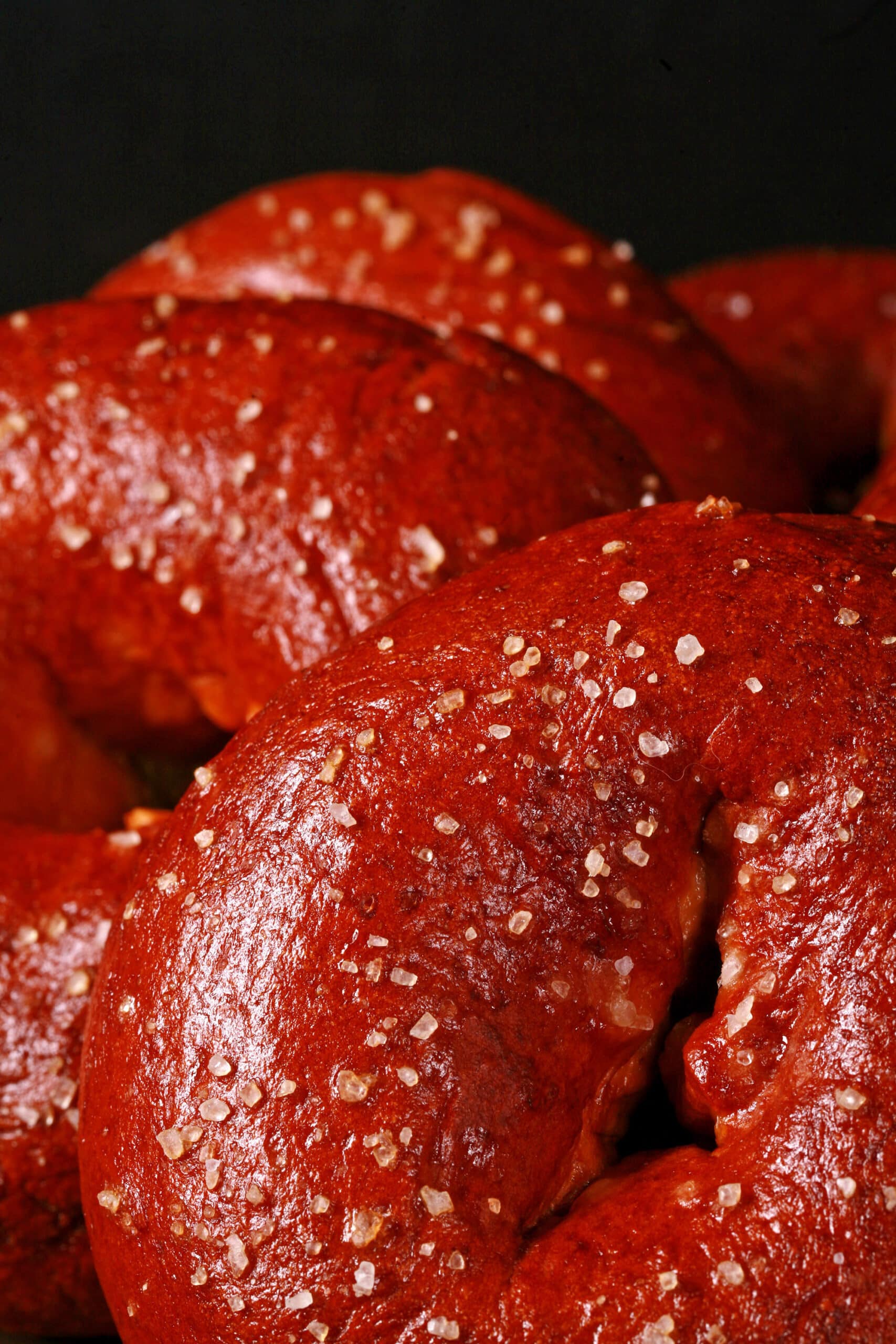 Close up view of pretzel bagels on a plate. They’re dark reddish brown and topped with salt.