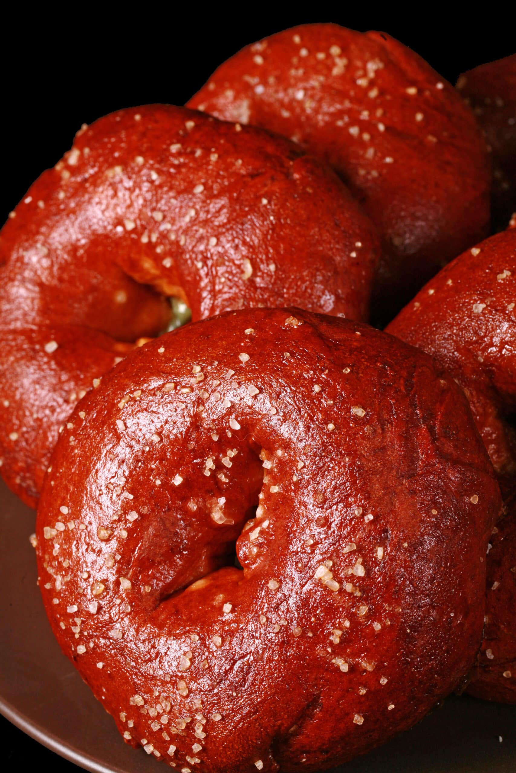 Close up view of pretzel bagels on a plate. They’re dark reddish brown and topped with salt.