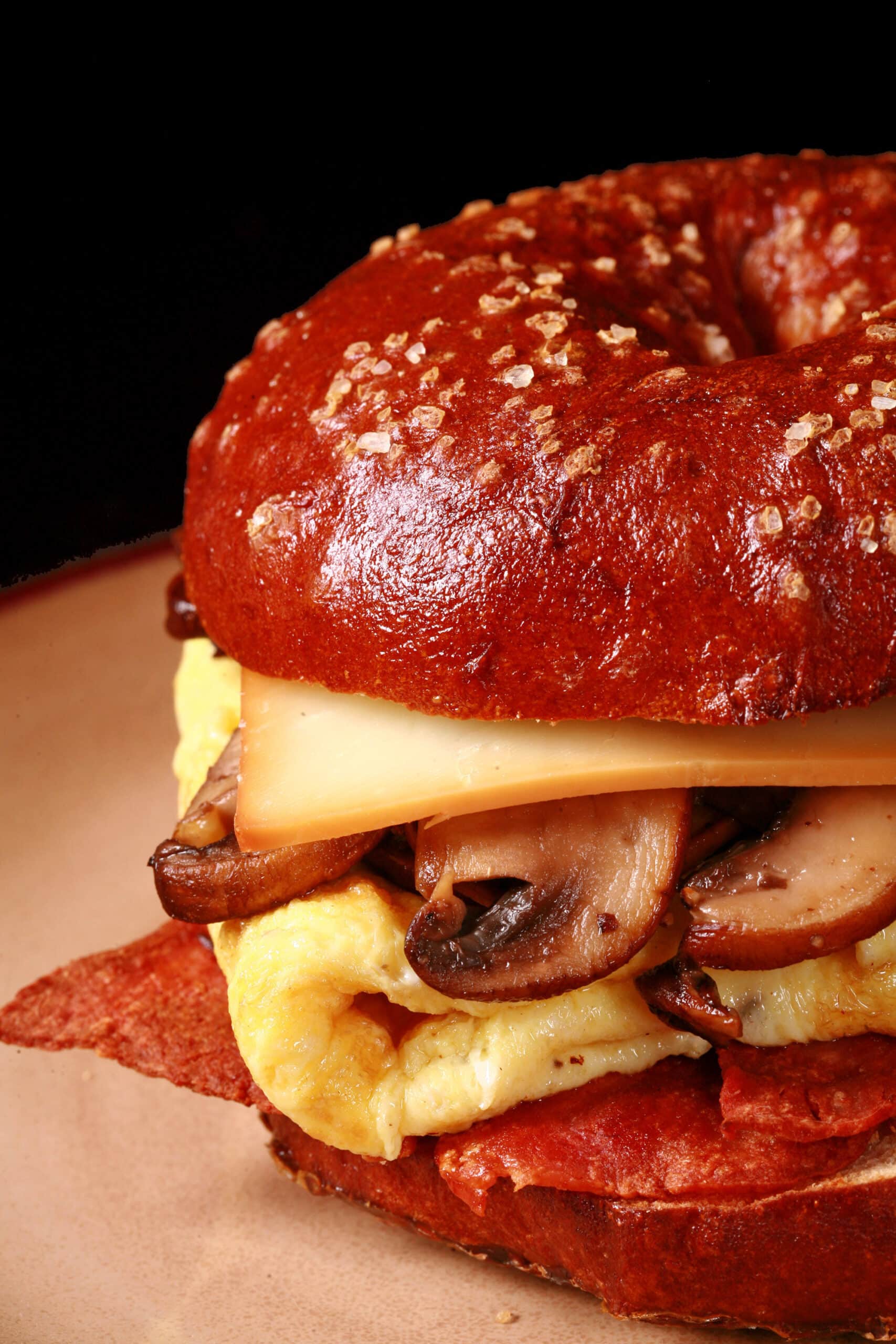 A breakfast sandwich made with a pretzel bagel, omelette, mushrooms, bacon, and cheese.