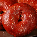 Close up view of pretzel bagels on a plate. They're dark reddish brown and topped with salt.