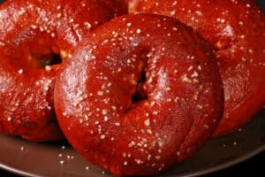 Close up view of pretzel bagels on a plate. They're dark reddish brown and topped with salt.