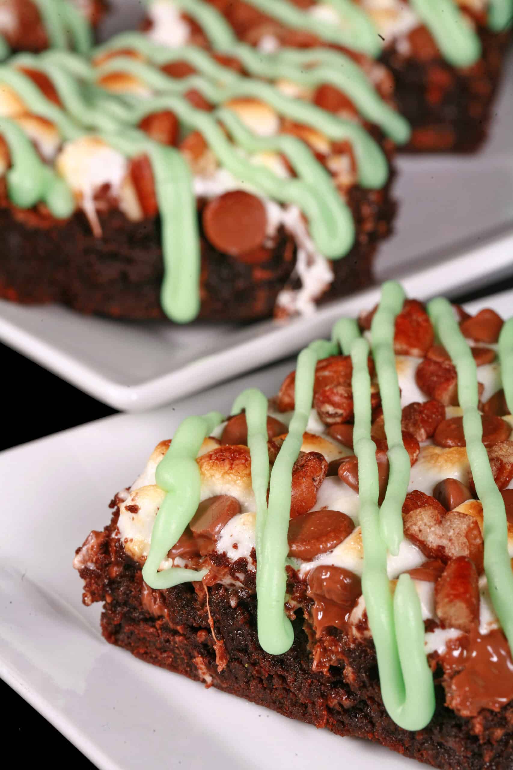 A plate of St Patrick’s Day rocky road brownies topped with toasted marshmallows, pecans, chocolate chips, and green tinted icing.