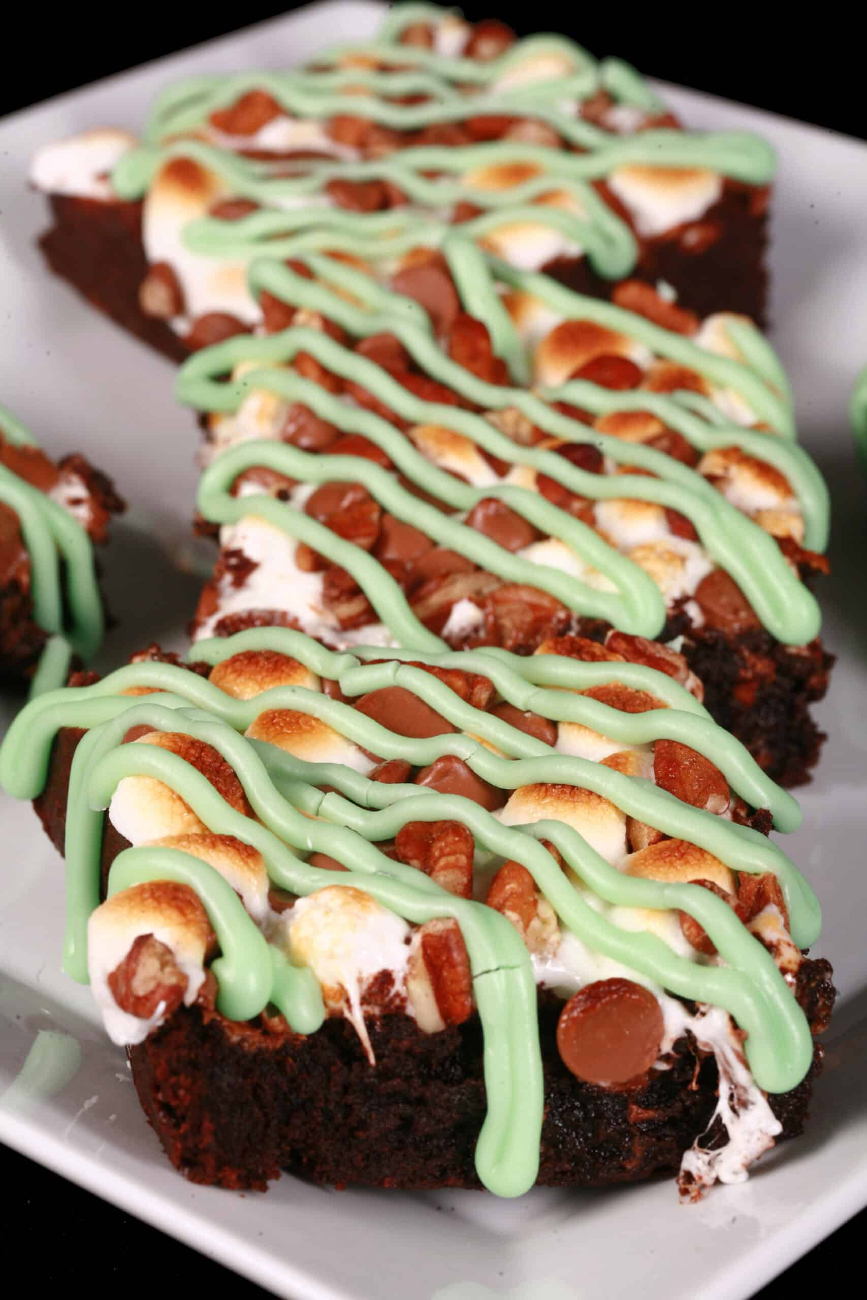 A plate of rocky road whiskey brownies topped with toasted marshmallows, pecans, chocolate chips, and green tinted icing.