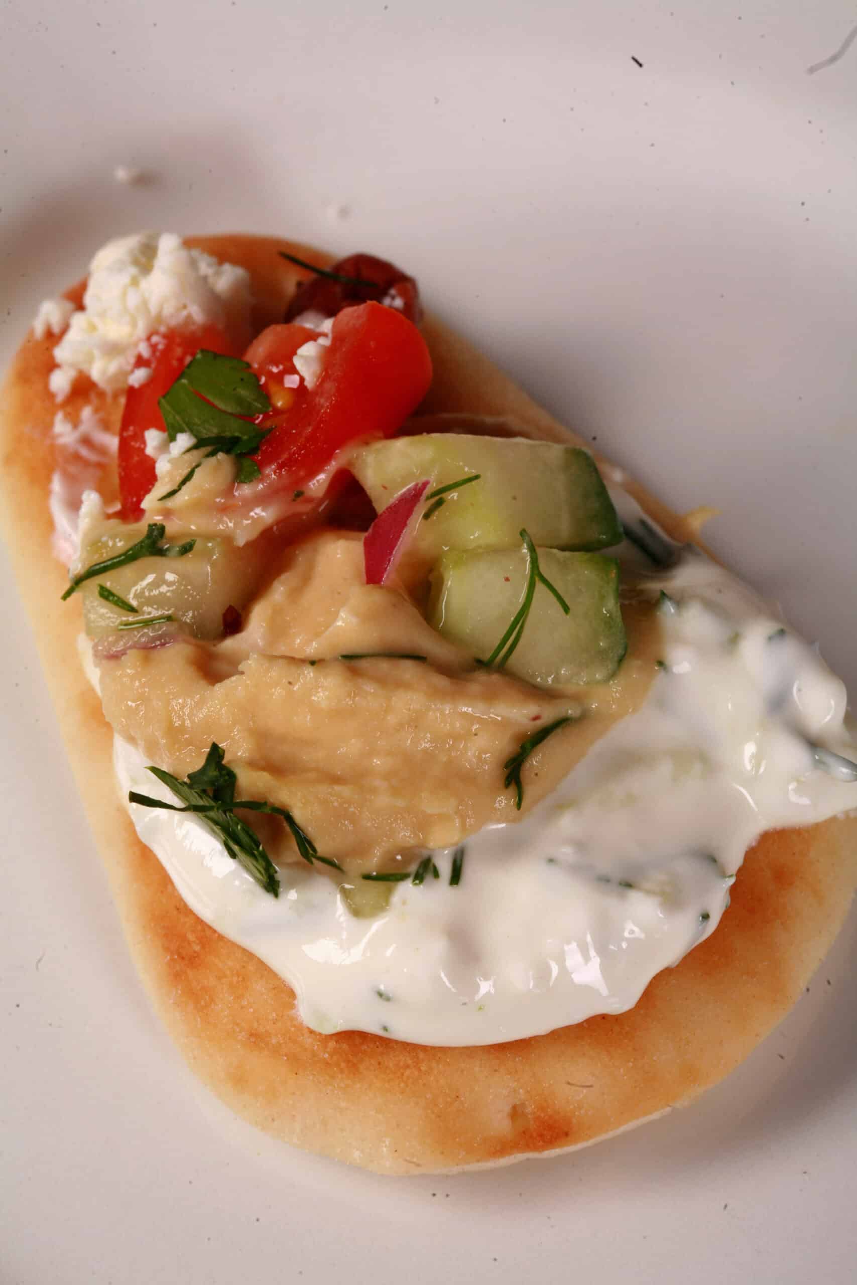 A small dipping wedge of pita, with layered Greek dip on it.