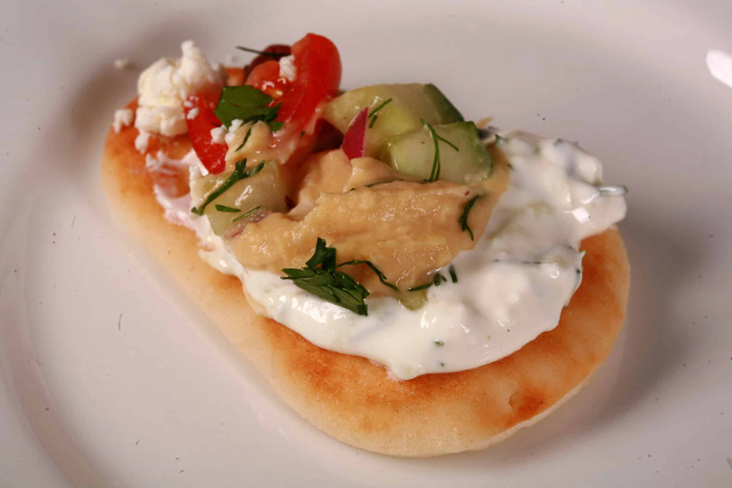 A small dipping wedge of pita, with layered Greek dip on it.