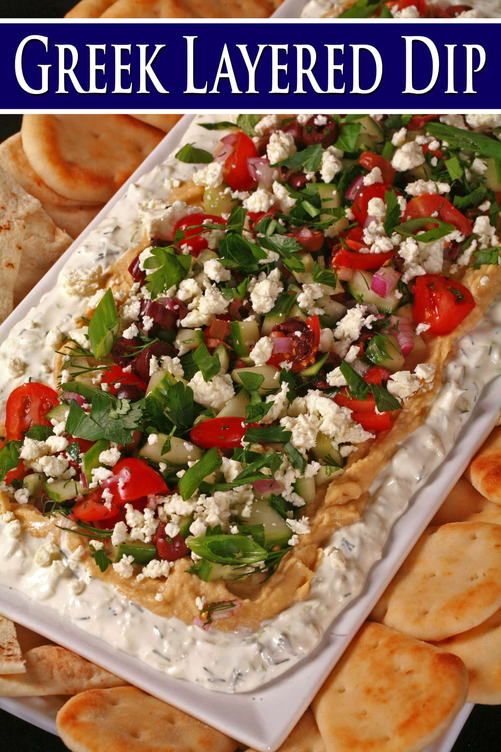 A plate of layered  Greek Dip, with Tzatziki cream cheese dip, hummus, a Greek salsa made of olives, cherry tomatoes, red onions, cucumber and fresh herbs, topped with feta.  Overlaid text says Greek Layered Dip.