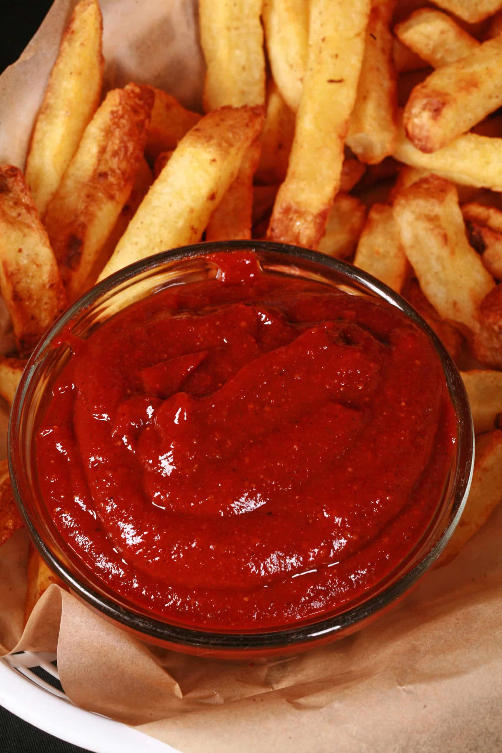 A small bowl of all dressed ketchup, in front of a of fries.