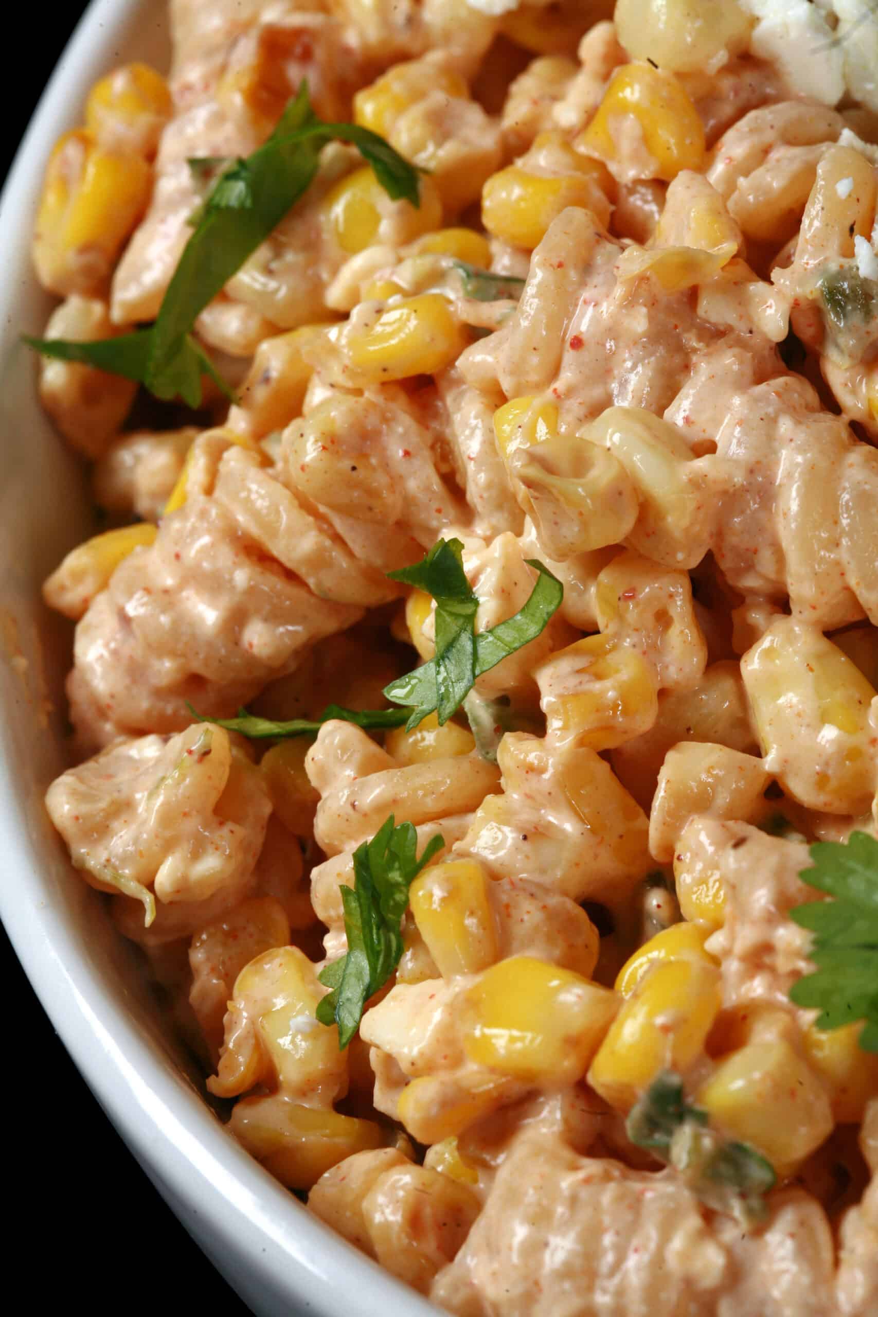 A bowl of Mexican street corn pasta salad, with rotini pasta, charred corn, crumbled cheese, green onions, and jalapenos in a creamy dressing.