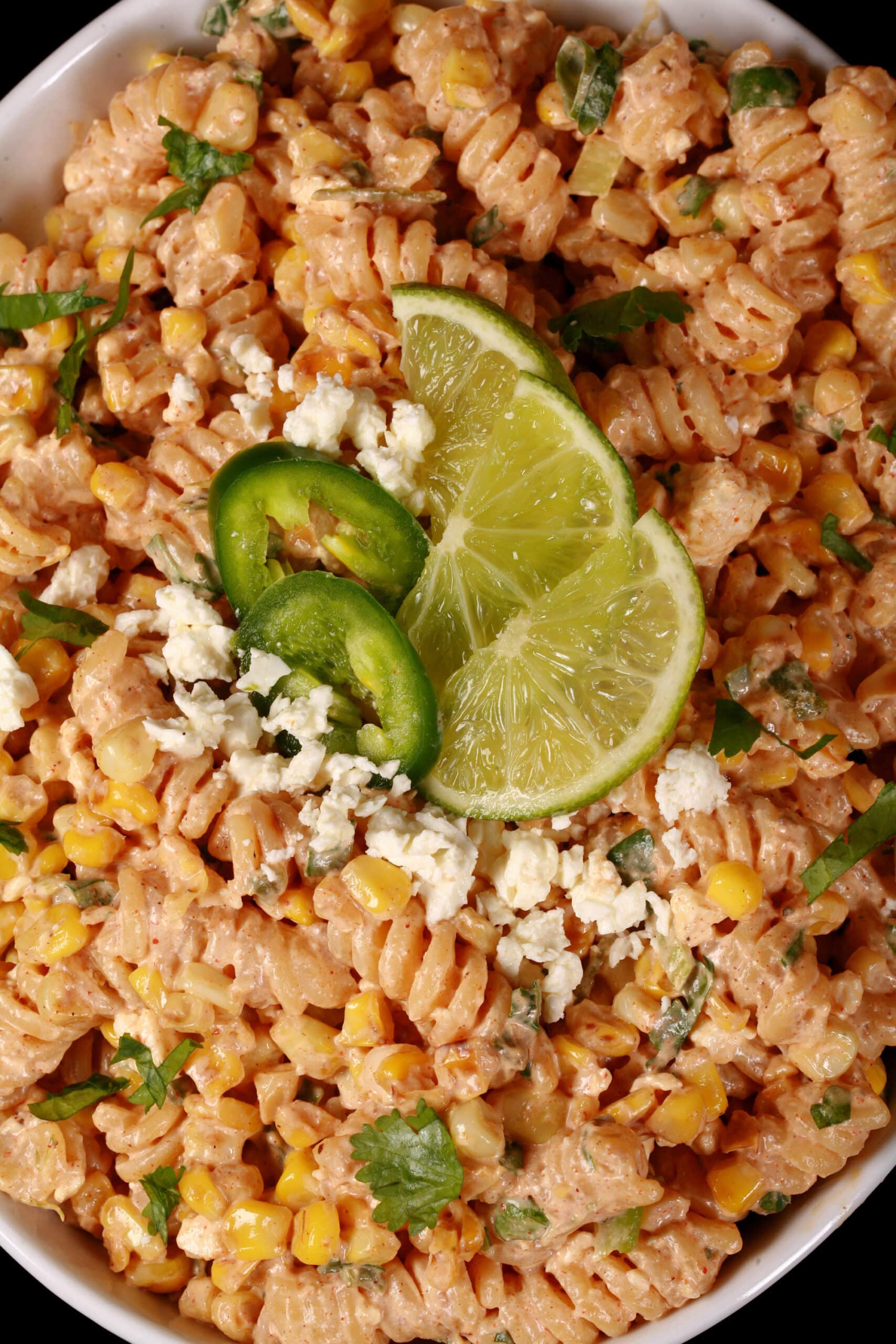 A bowl of elote pasta salad, with rotini pasta, charred corn, crumbled cheese, green onions, and jalapenos in a creamy dressing.