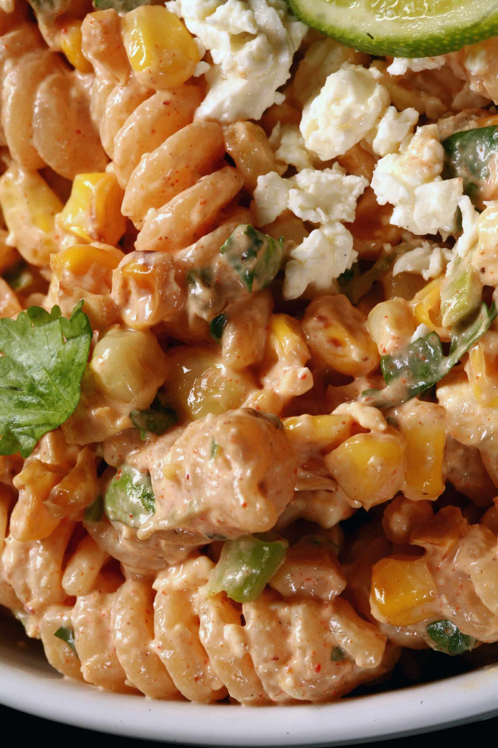 A bowl of esquites pasta salad, with rotini pasta, charred corn, crumbled cheese, green onions, and jalapenos in a creamy dressing.