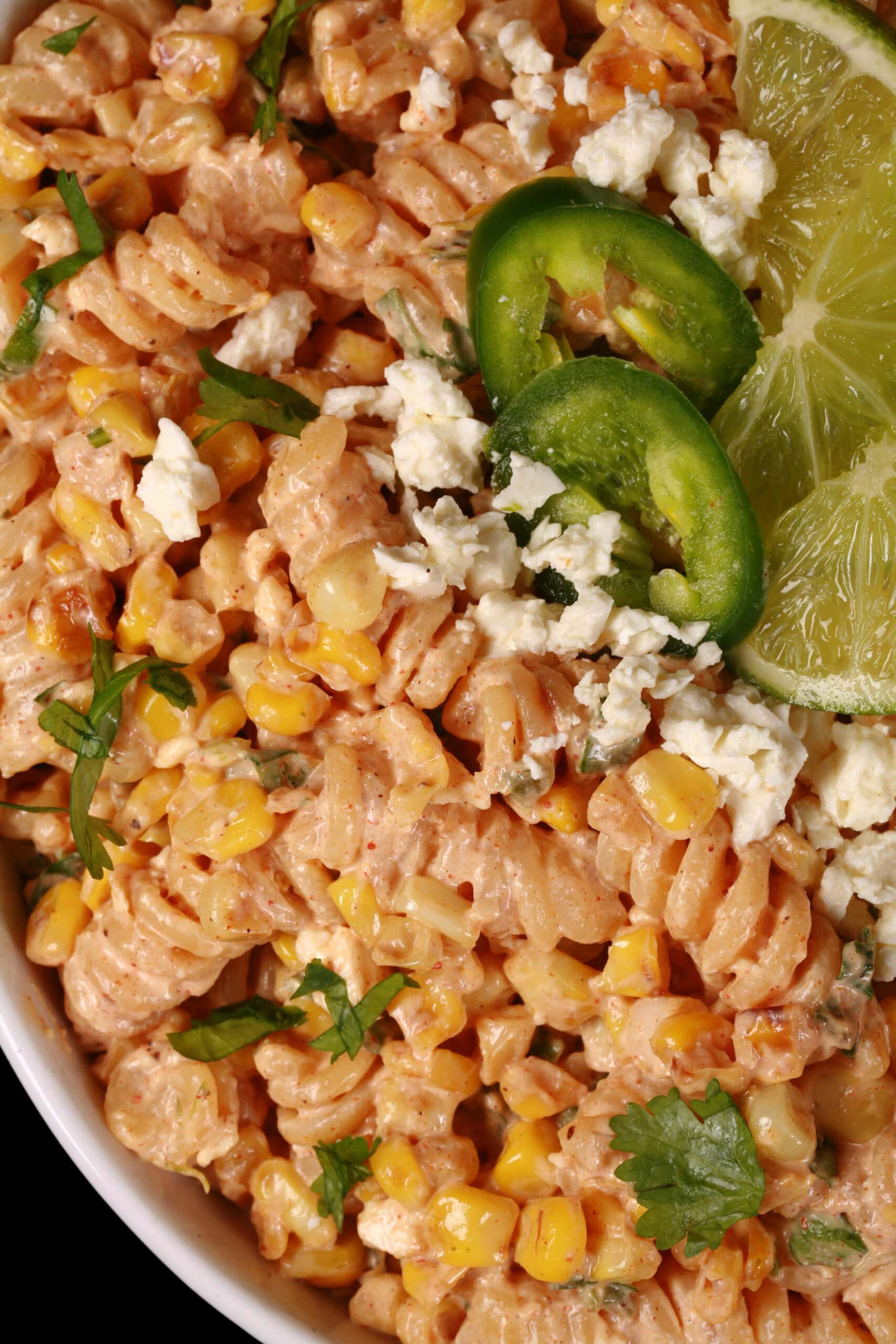 A bowl of Mexican street corn pasta salad, with rotini pasta, charred corn, crumbled cheese, green onions, and jalapenos in a creamy dressing.