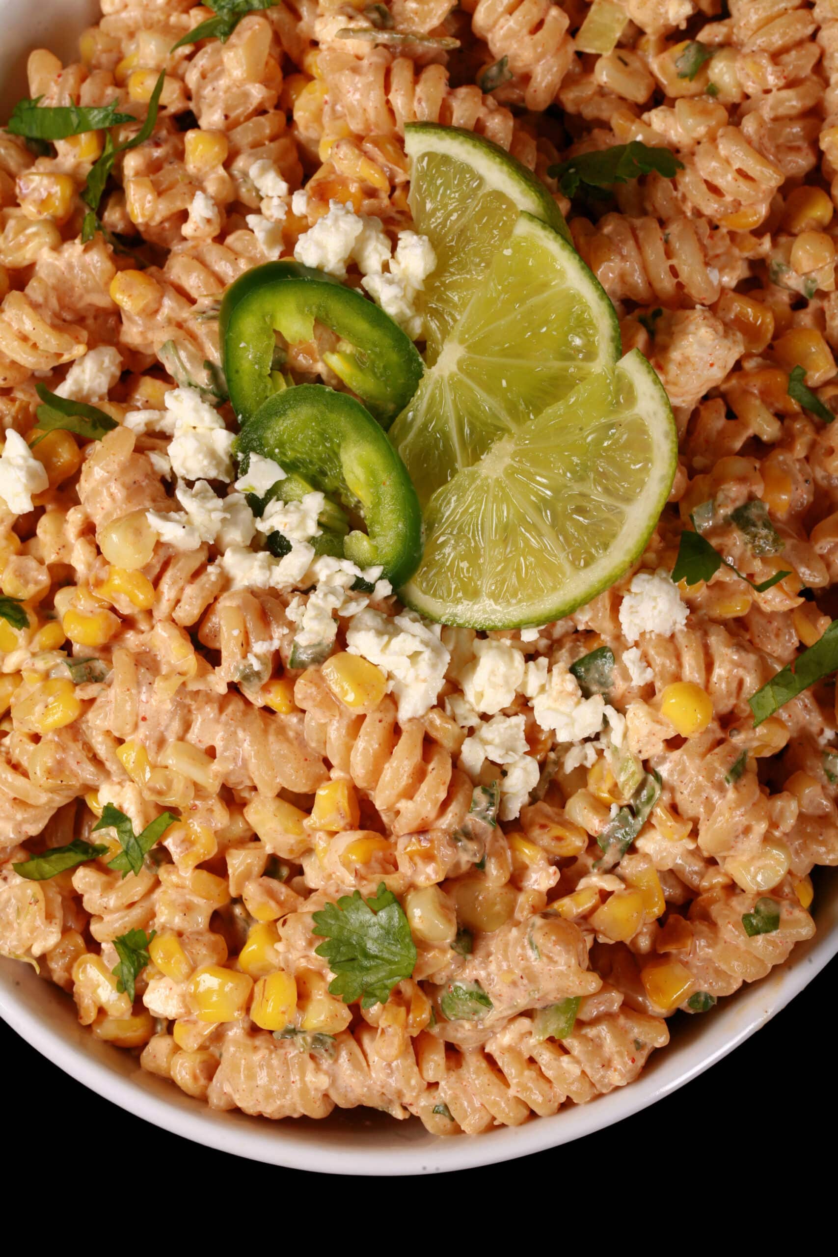 A bowl of elote pasta salad, with rotini pasta, charred corn, crumbled cheese, green onions, and jalapenos in a creamy dressing.