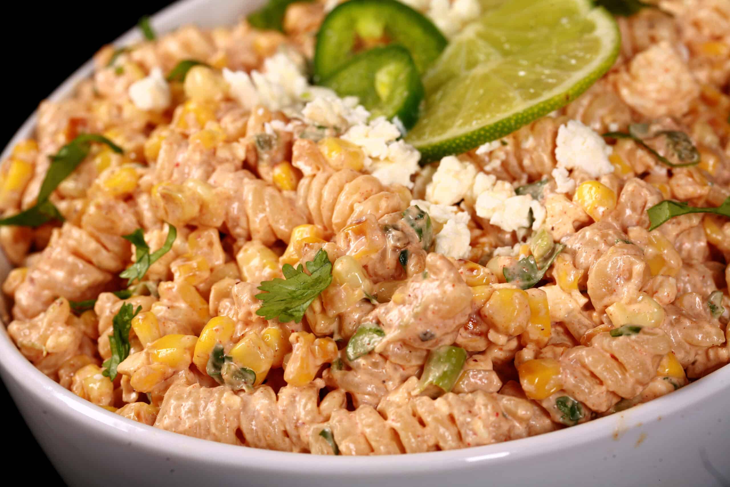 A bowl of esquites pasta salad, with rotini pasta, charred corn, crumbled cheese, green onions, and jalapenos in a creamy dressing.