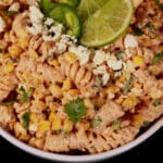 A bowl of Mexican street corn pasta salad, with rotini pasta, charred corn, crumbled cheese, green onions, and jalapenos in a creamy dressing.