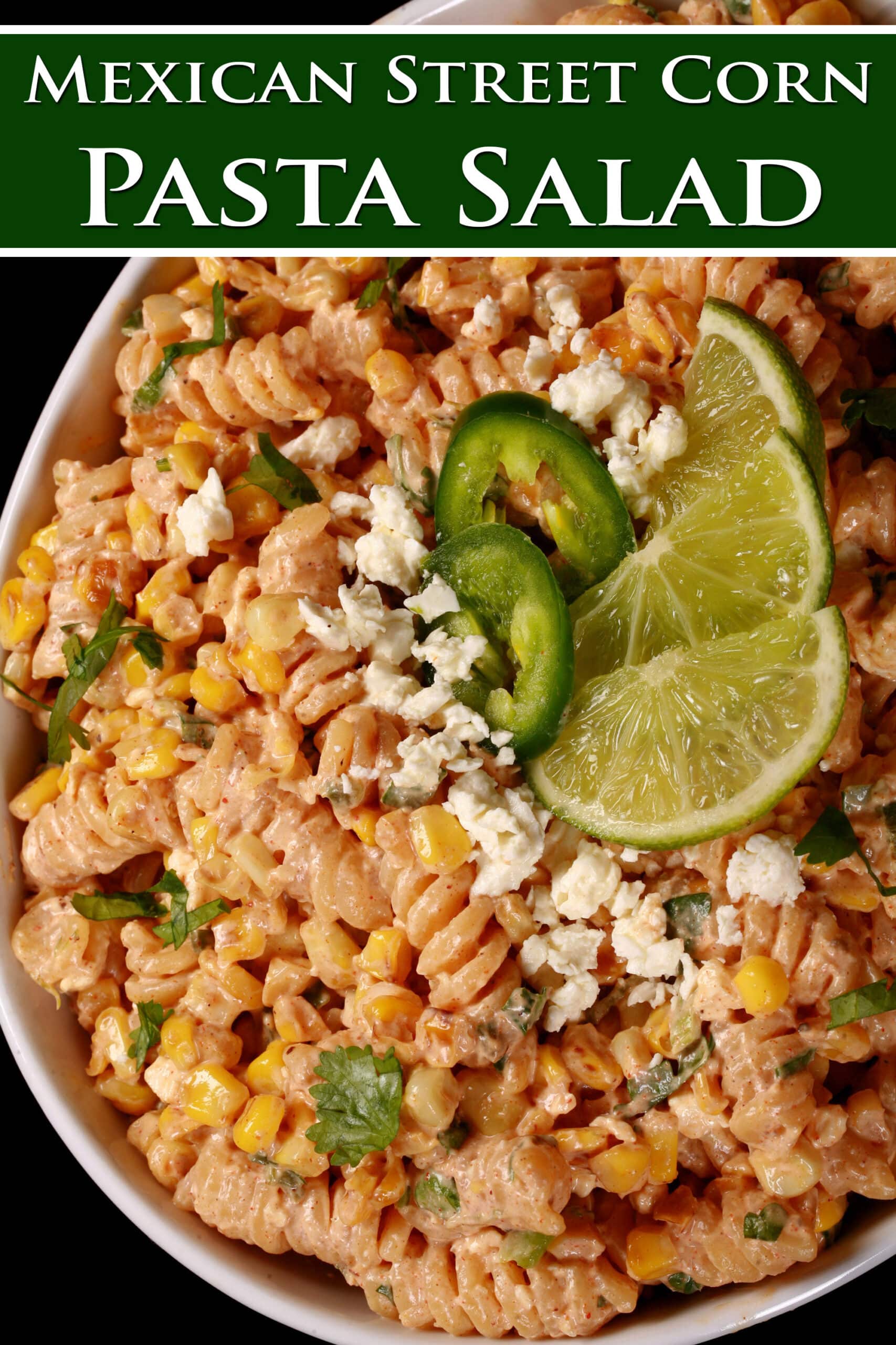 A bowl of elote pasta salad, with rotini pasta, charred corn, crumbled cheese, green onions, and jalapenos in a creamy dressing. Overlaid text says Mexican Street Corn Pasta Salad.