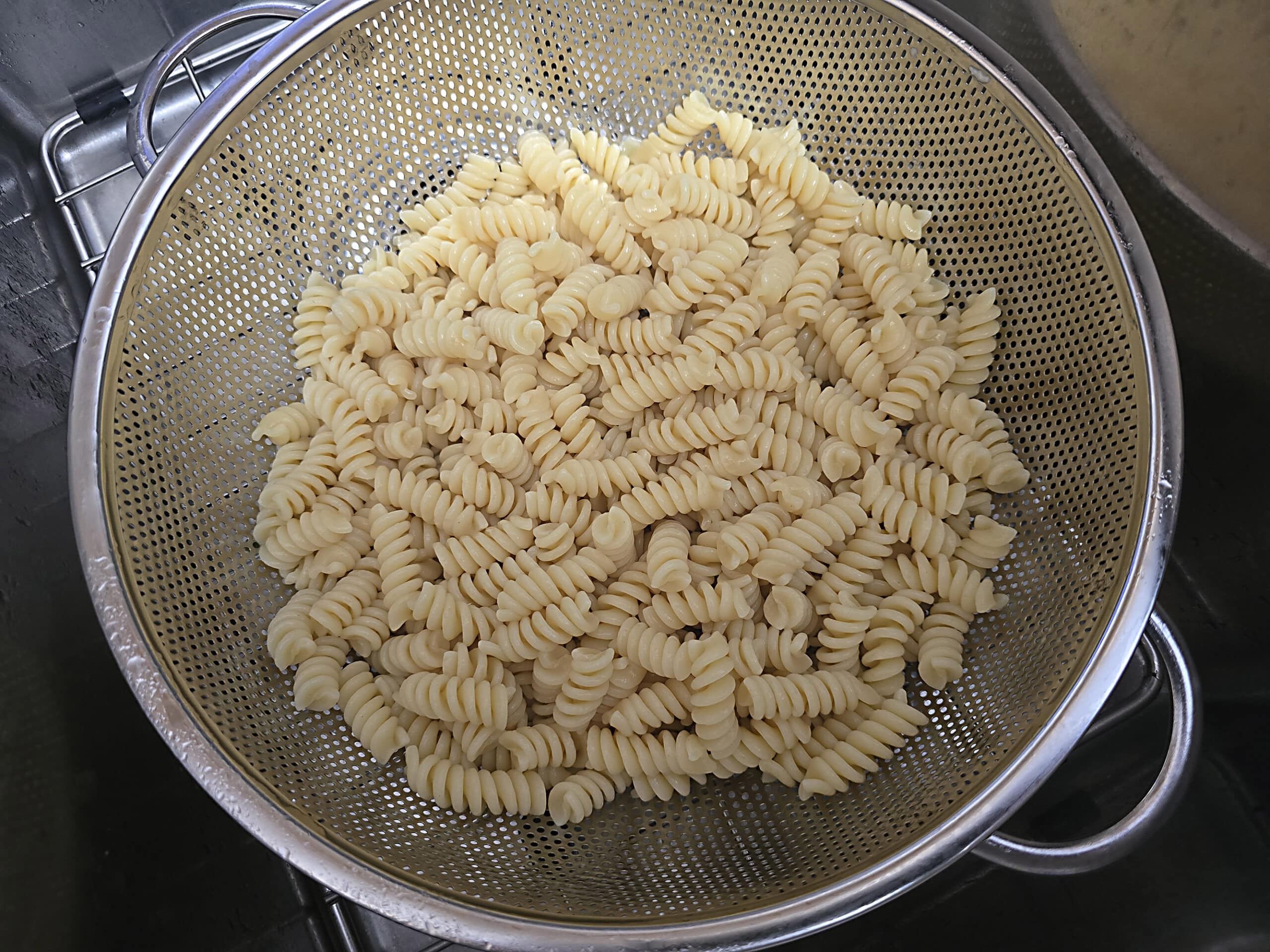 A colander of rotini pasta in a sink.