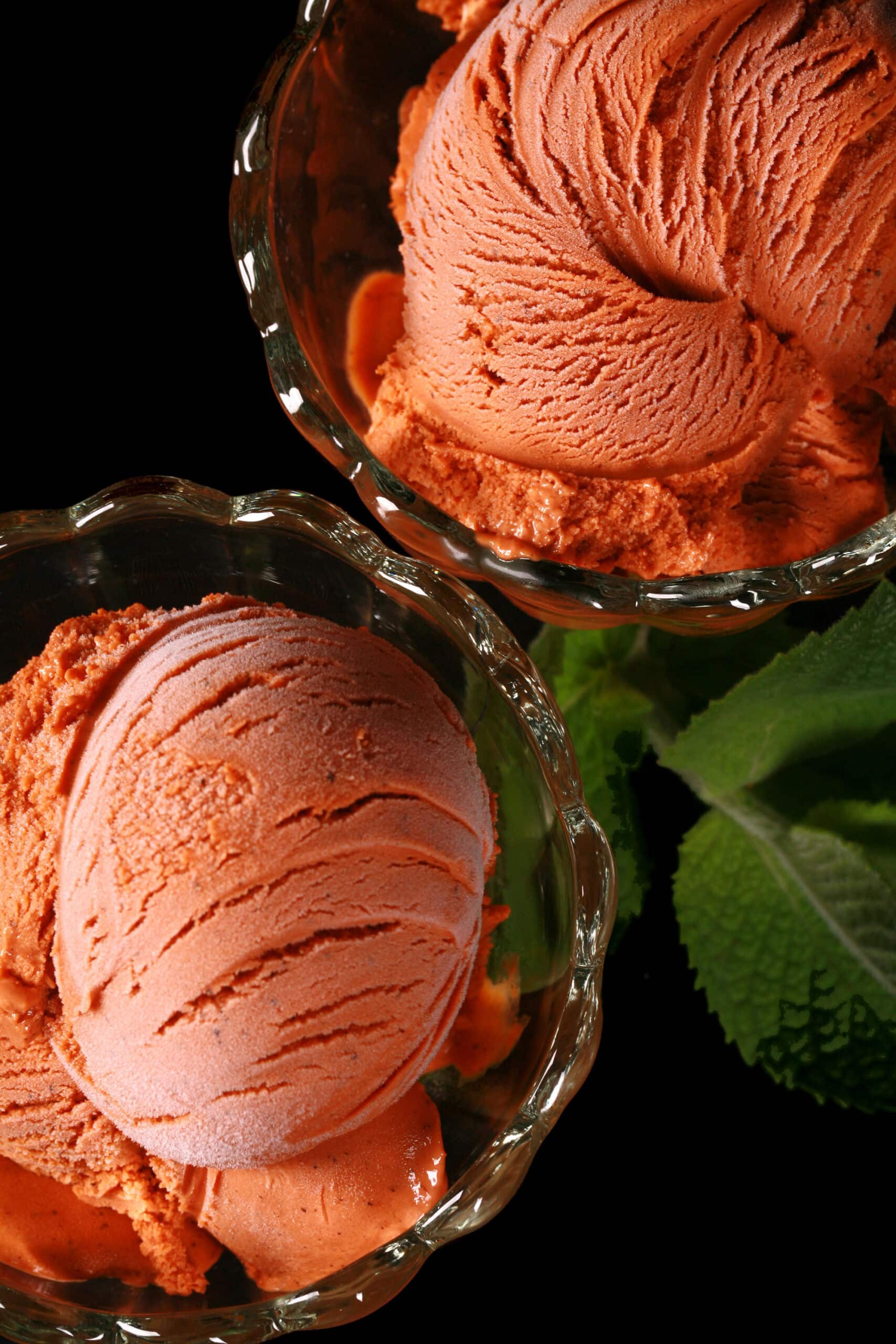 2 bowls of Thai tea ice cream in glass bowls, with fresh mint next to them.