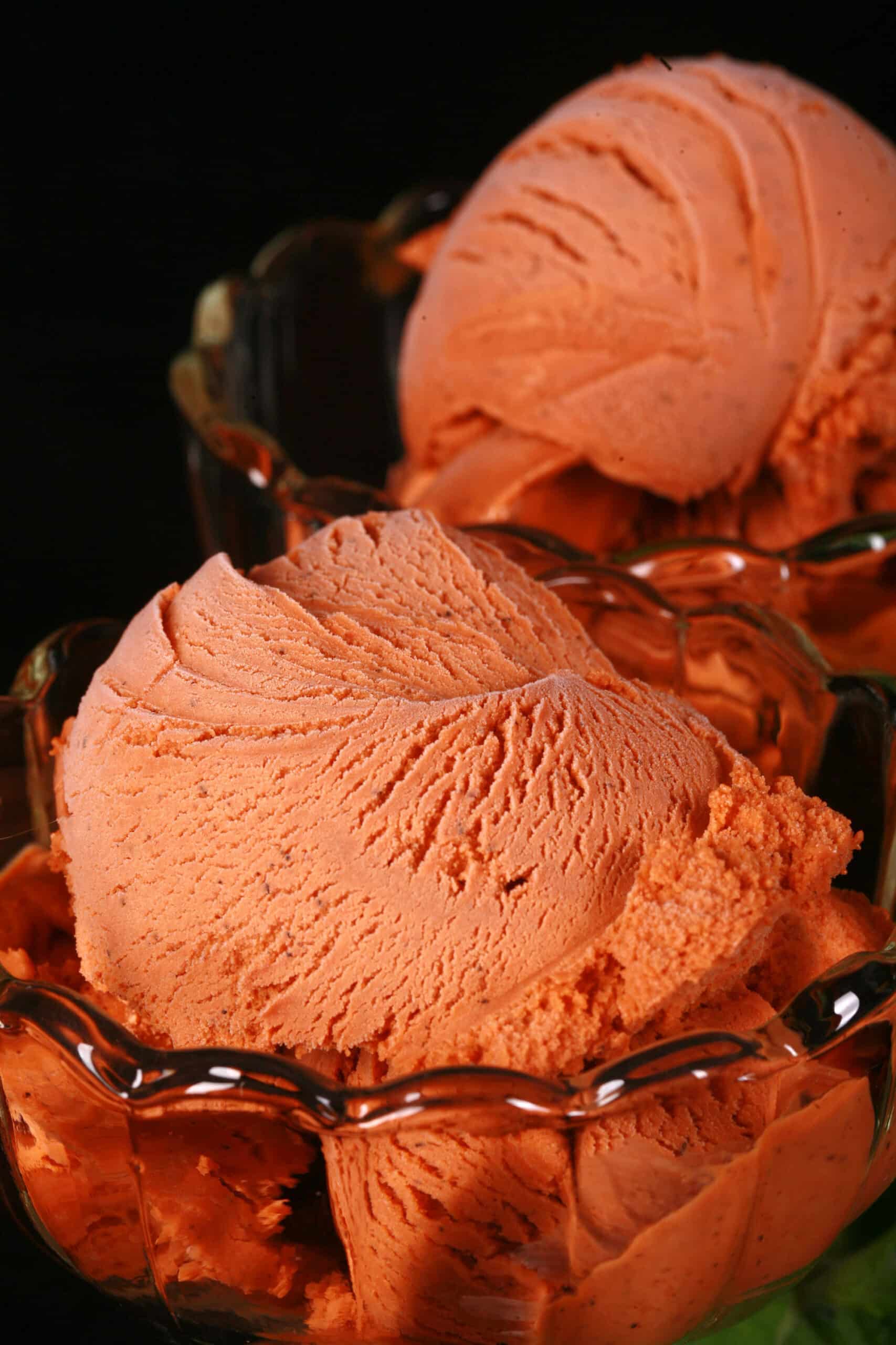 2 bowls of Thai tea ice cream in glass bowls, with fresh mint next to them.