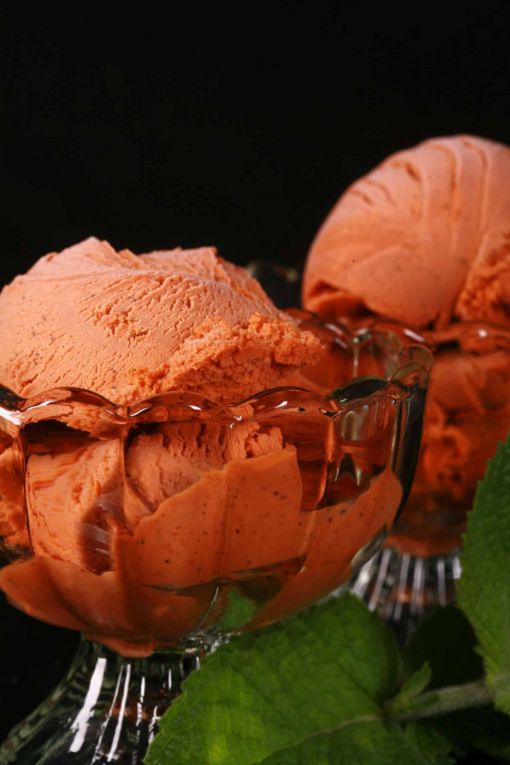 2 bowls of Thai tea ice cream in glass bowls, with fresh mint next to them.