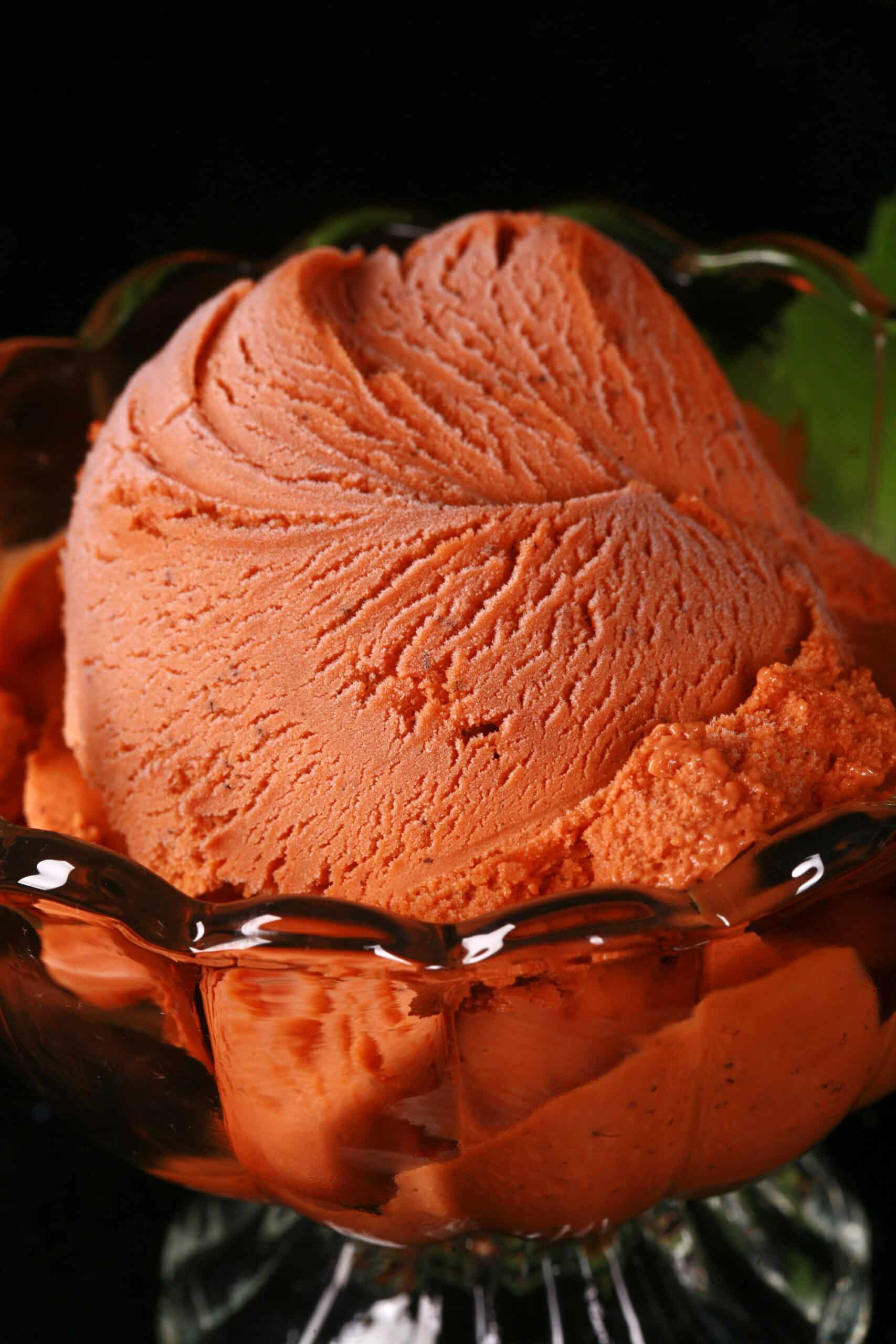 A bowl of Thai iced tea ice cream in a glass bowls, with fresh mint next to it.