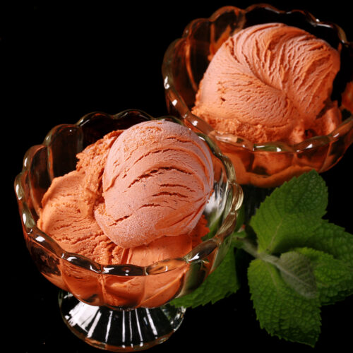 2 bowls of Thai tea ice cream in glass bowls, with fresh mint next to them.