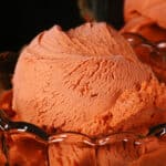 2 bowls of Thai tea ice cream in glass bowls, with fresh mint next to them.