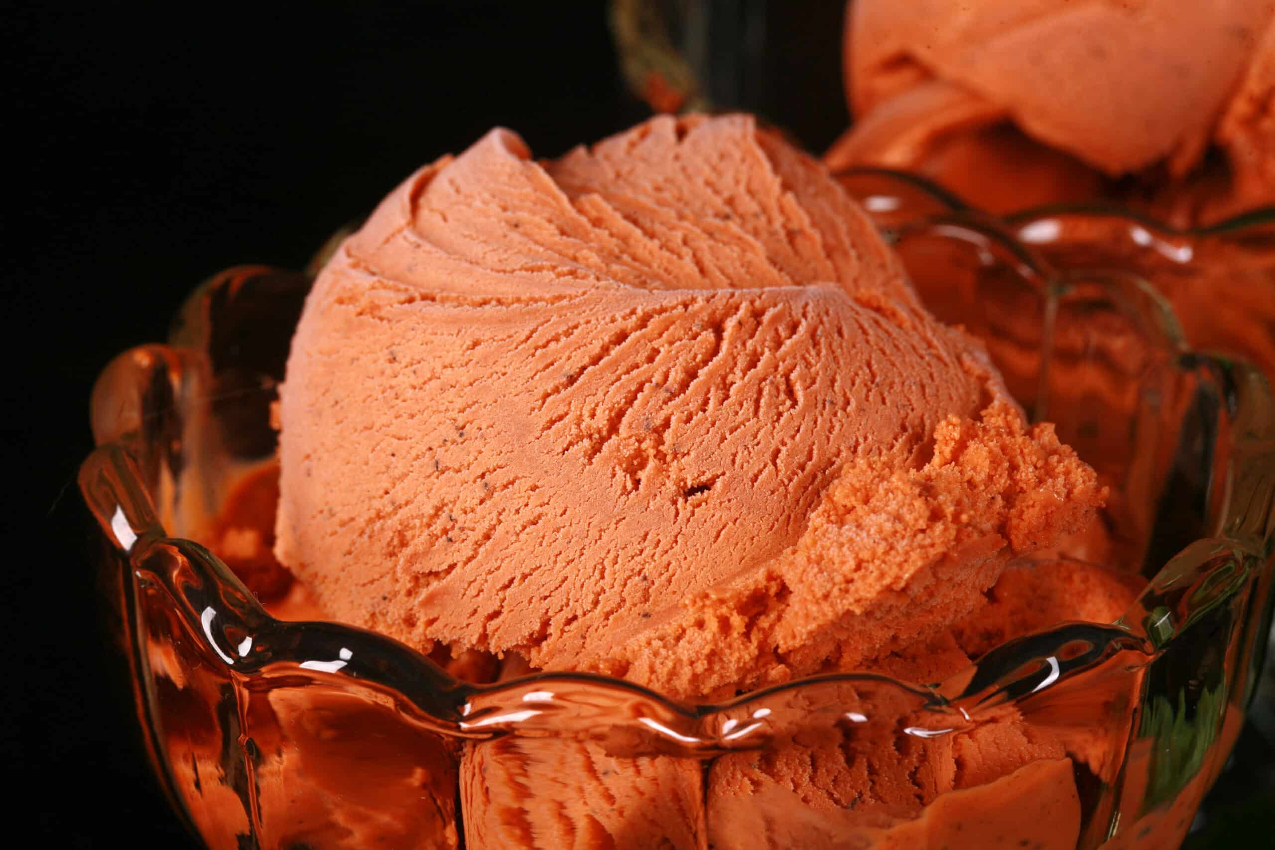 2 bowls of Thai tea ice cream in glass bowls, with fresh mint next to them.