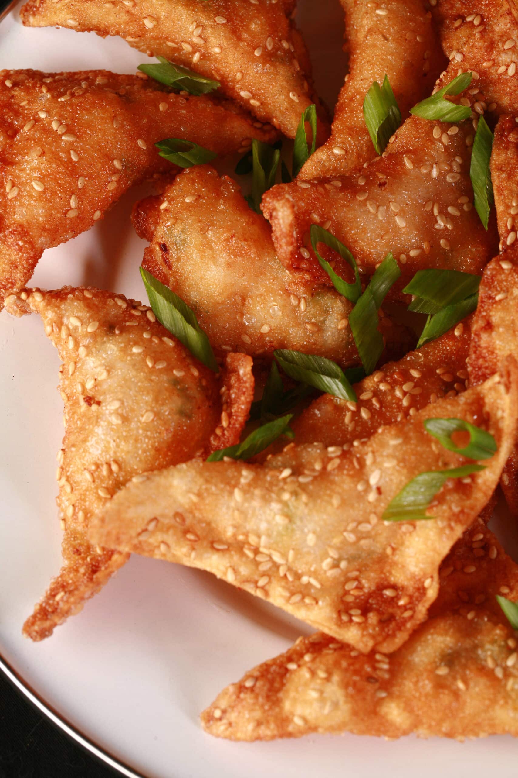A plate of deep fried shrimp wontons with sesame seeds and green onions on them.