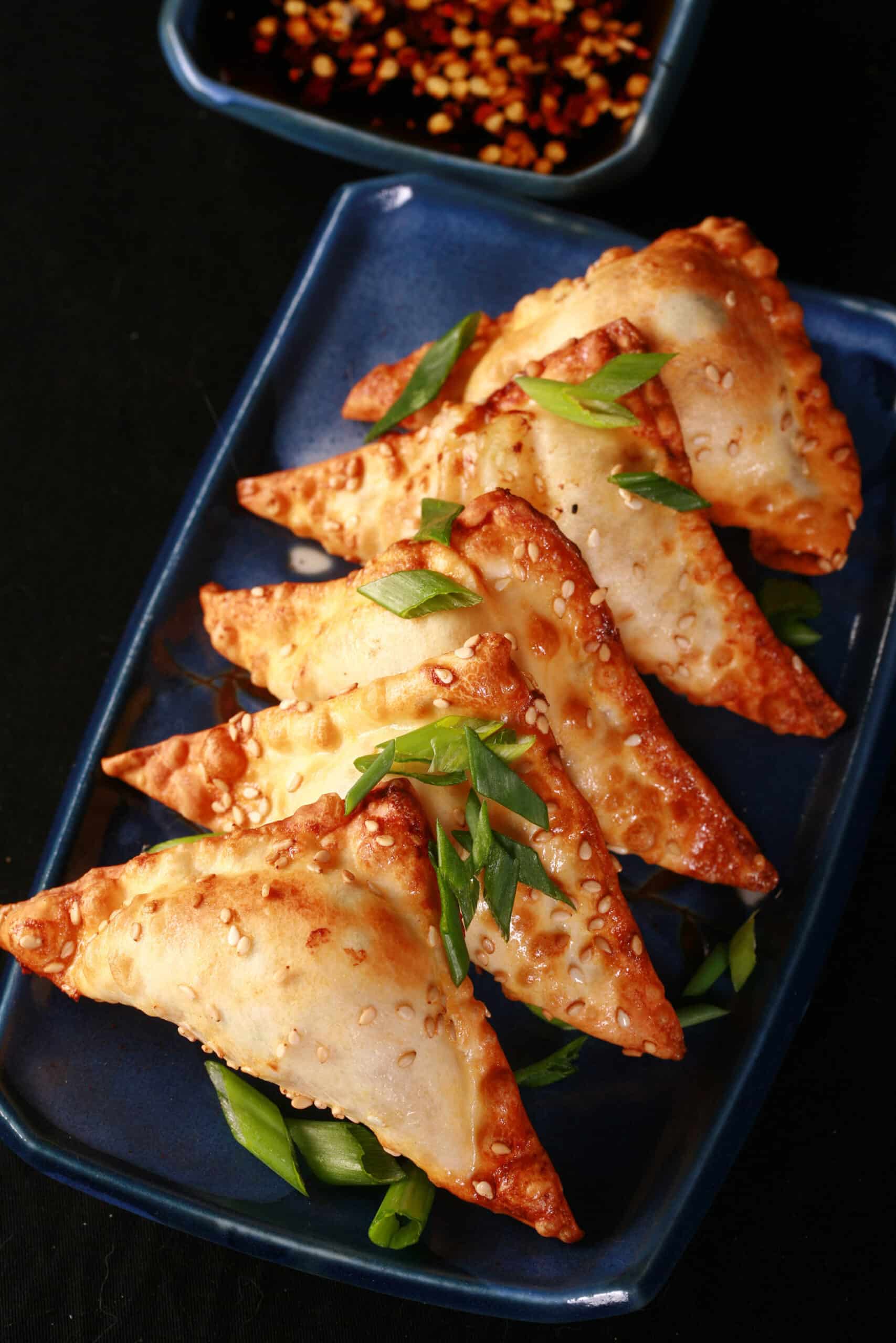 A plate of air fried shrimp wontons with sesame seeds and green onions on them, and dipping sauce on the side.