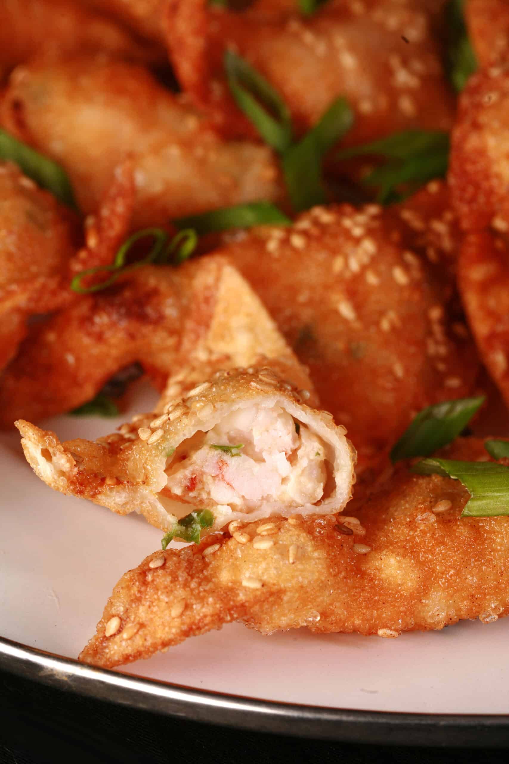 A plate of deep fried shrimp wontons with sesame seeds and green onions on them.