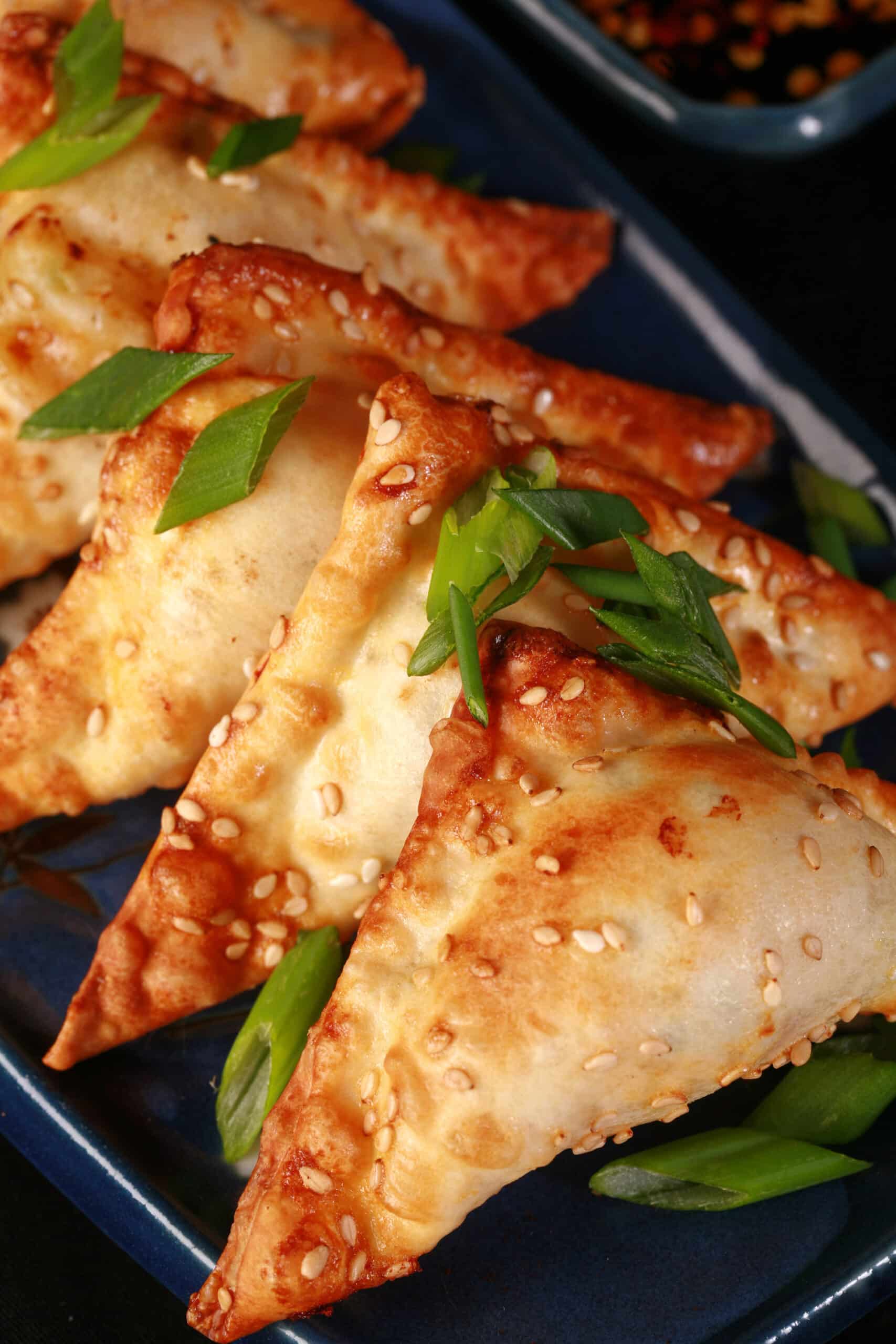 A plate of air fried shrimp wontons with sesame seeds and green onions on them, and dipping sauce on the side.