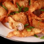 A plate of deep fried shrimp wontons with sesame seeds and green onions on them.