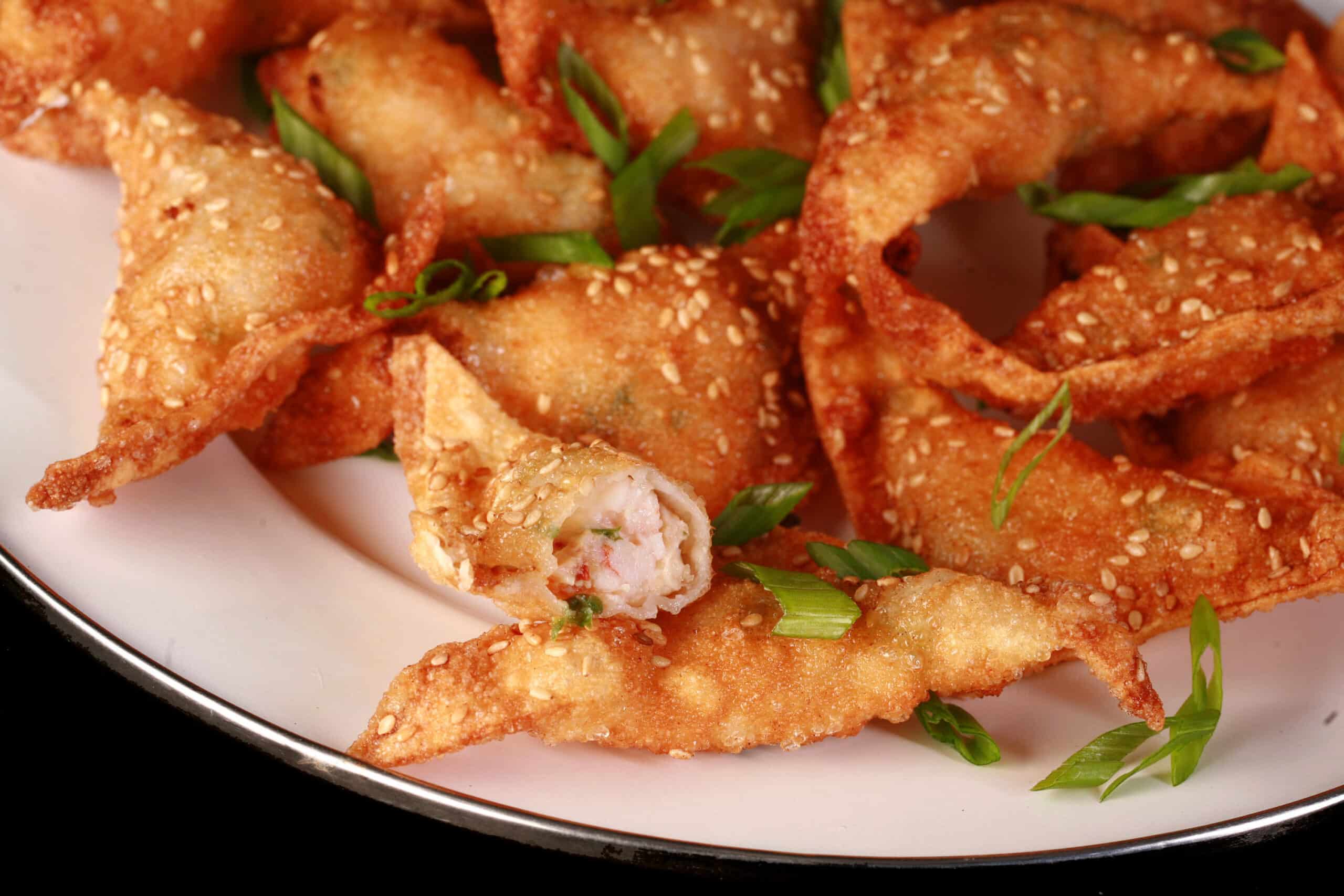 A plate of deep fried shrimp wontons with sesame seeds and green onions on them.