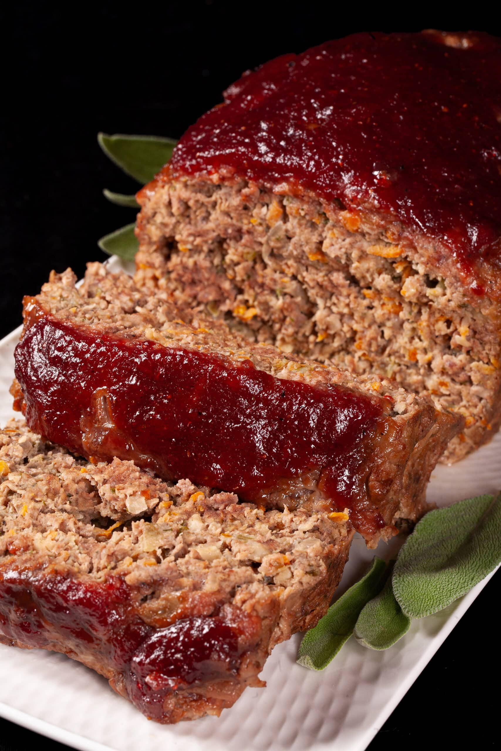 Venison meatloaf with carrots, mushrooms, celery bits, and herbs visible, topped with cranberry glaze.