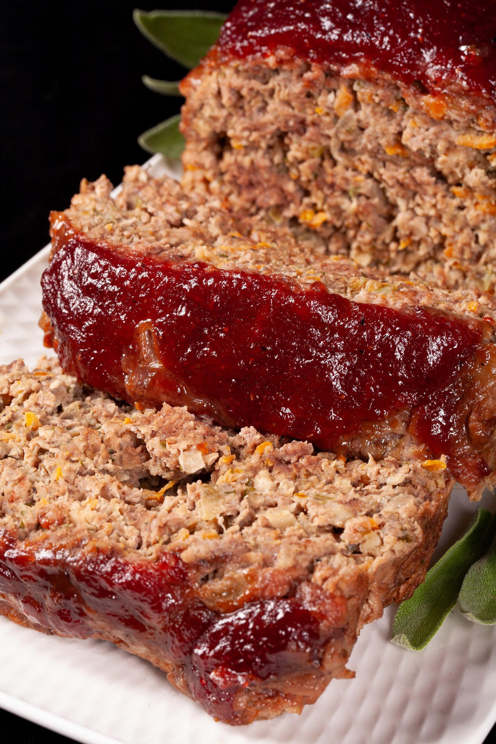 Venison meatloaf with carrots, mushrooms, celery bits, and herbs visible, topped with cranberry glaze.