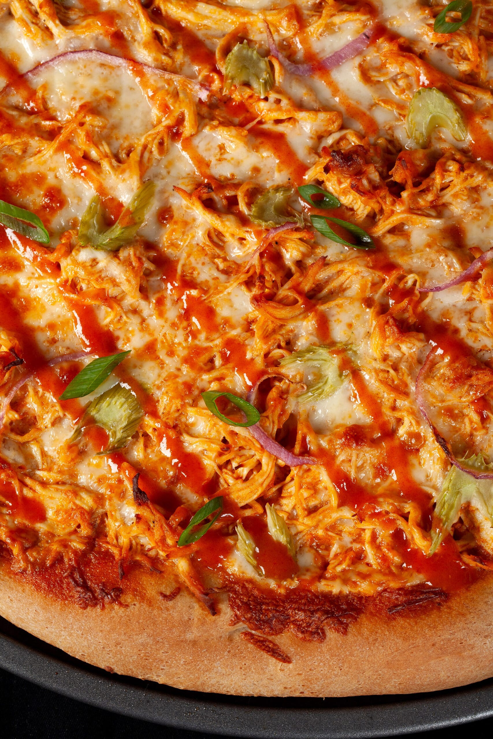 A buffalo chicken pizza with shredded chicken, celery, red onion, Monterey Jack cheese, hot sauce, and ranch dressing.