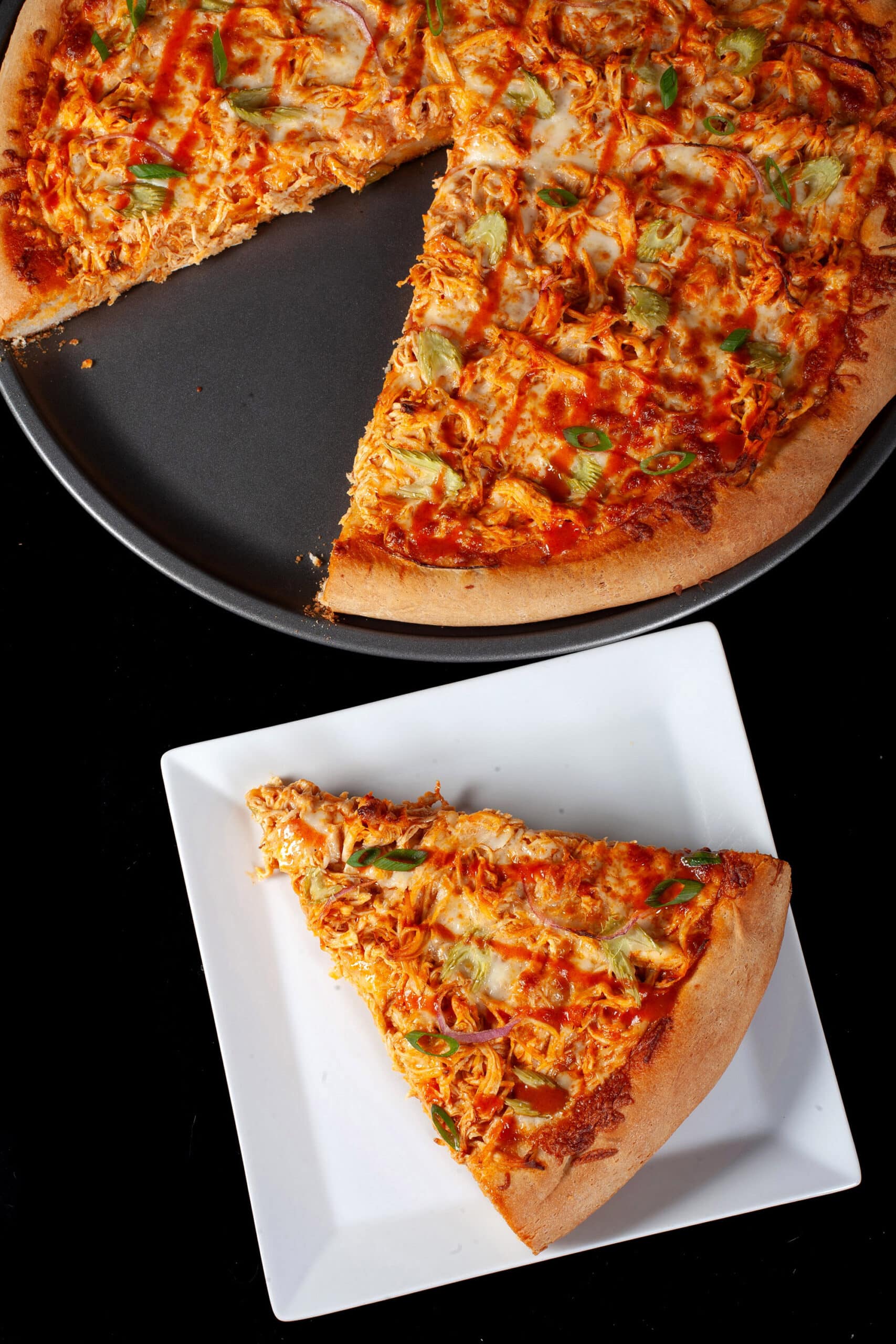 A buffalo wing pizza with shredded chicken, celery, red onion, Monterey Jack cheese, hot sauce, and ranch dressing.