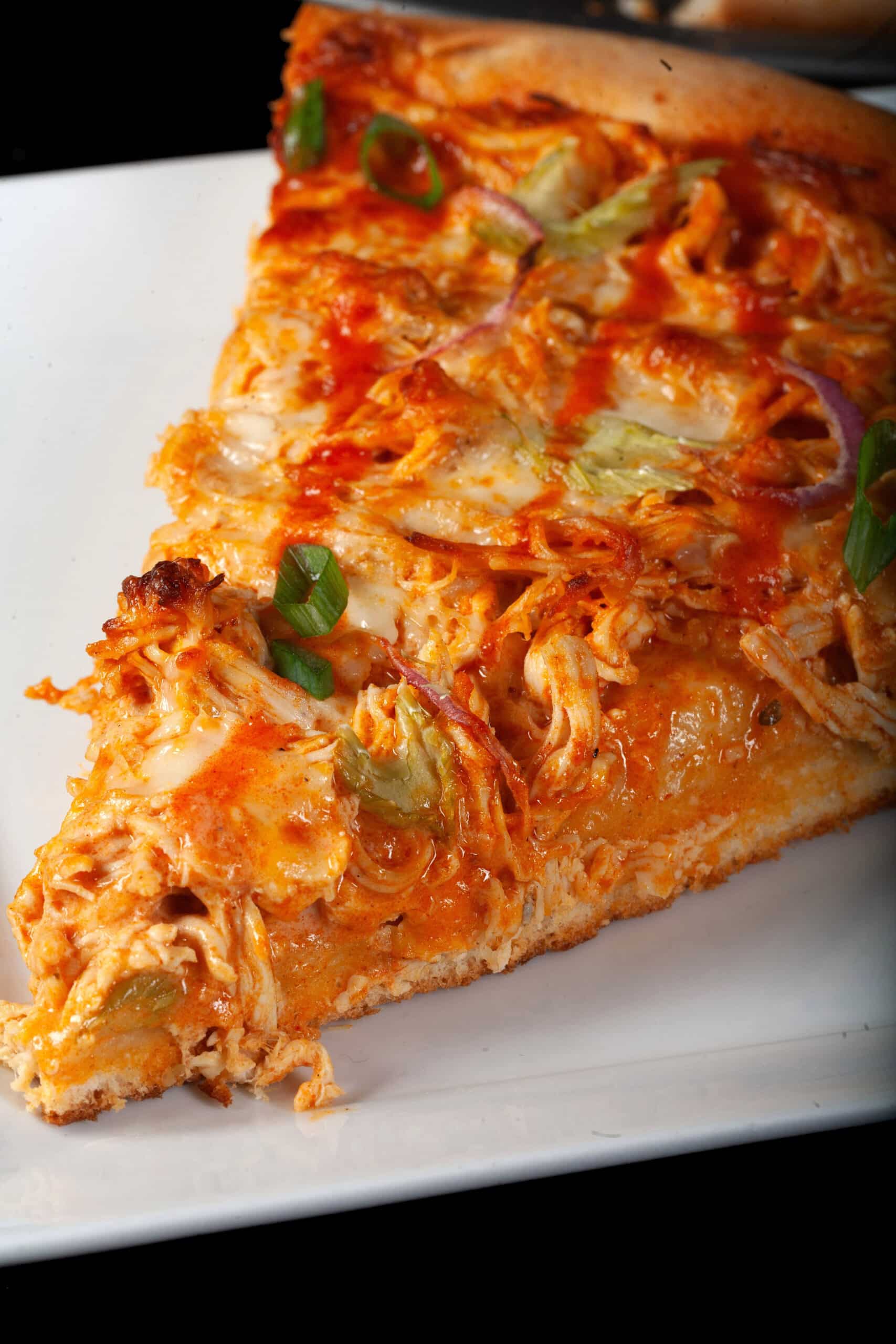 A slice of buffalo chicken pizza with shredded chicken, celery, red onion, Monterey Jack cheese, hot sauce, and ranch dressing.