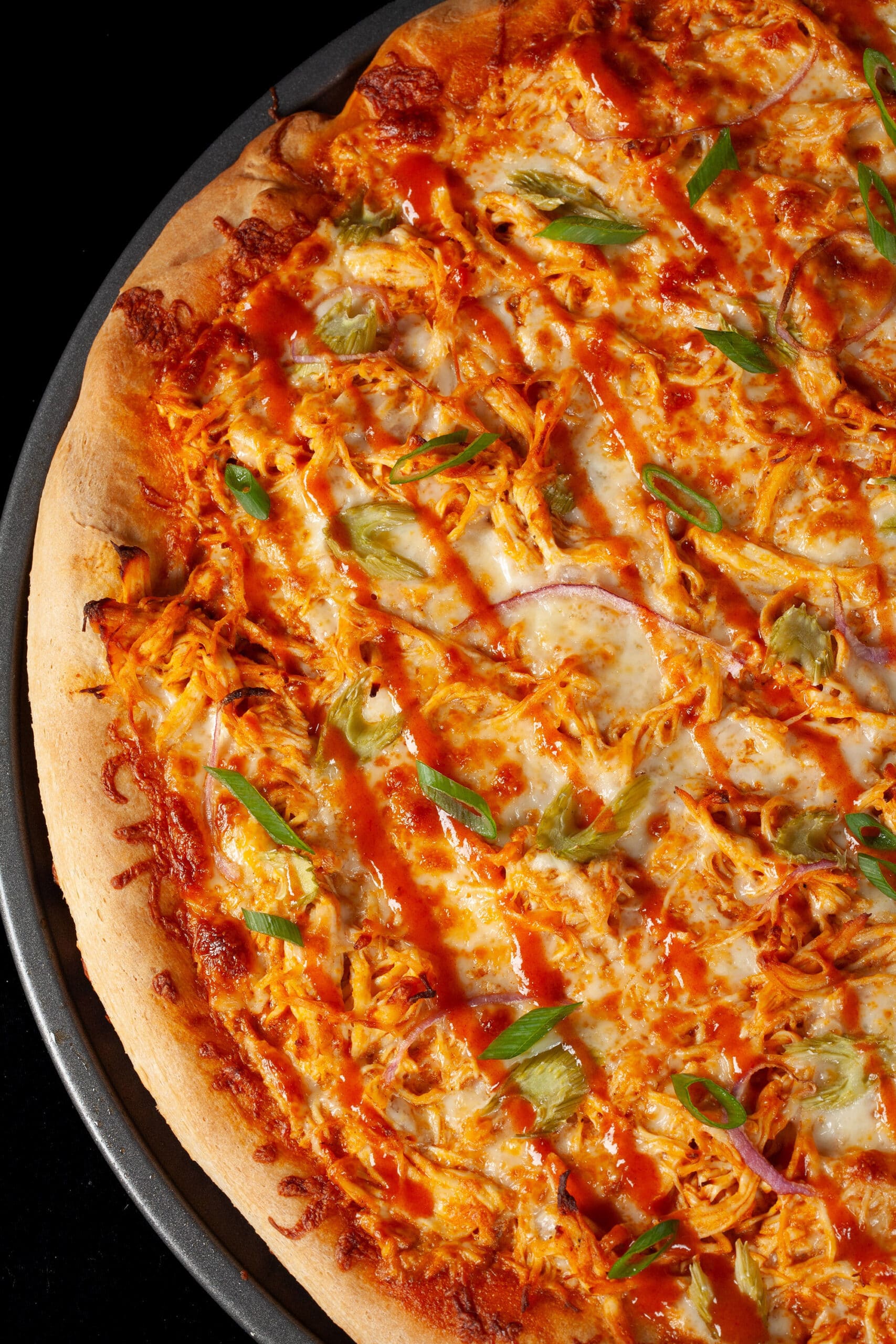 A buffalo wing pizza with shredded chicken, celery, red onion, Monterey Jack cheese, hot sauce, and ranch dressing.