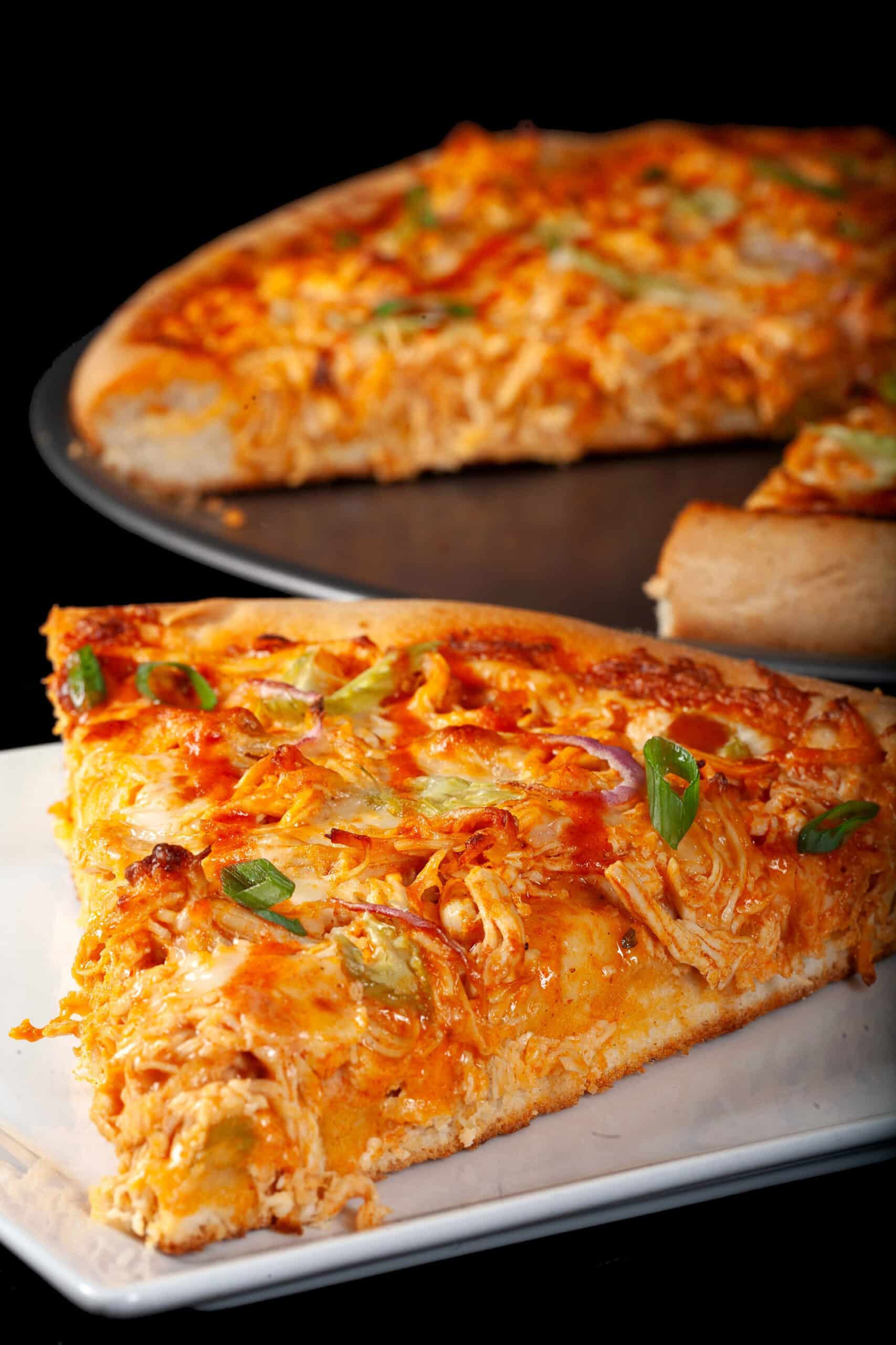 A slice of buffalo chicken pizza with shredded chicken, celery, red onion, Monterey Jack cheese, hot sauce, and ranch dressing.