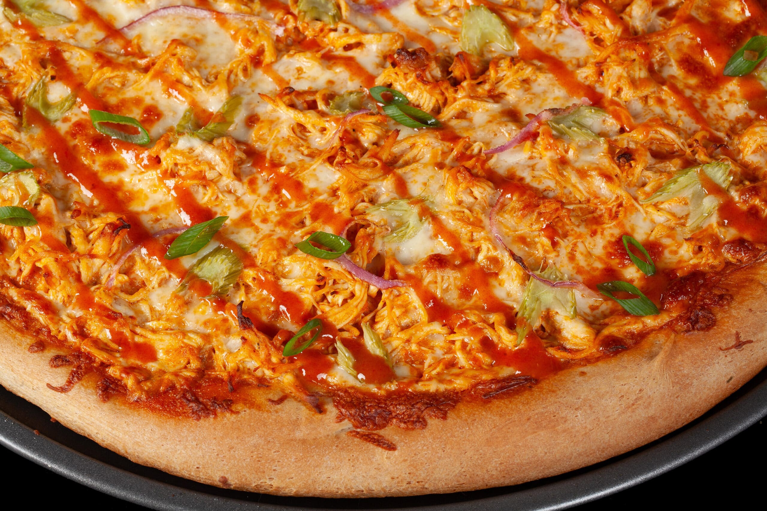 A buffalo wing pizza with shredded chicken, celery, red onion, Monterey Jack cheese, hot sauce, and ranch dressing.